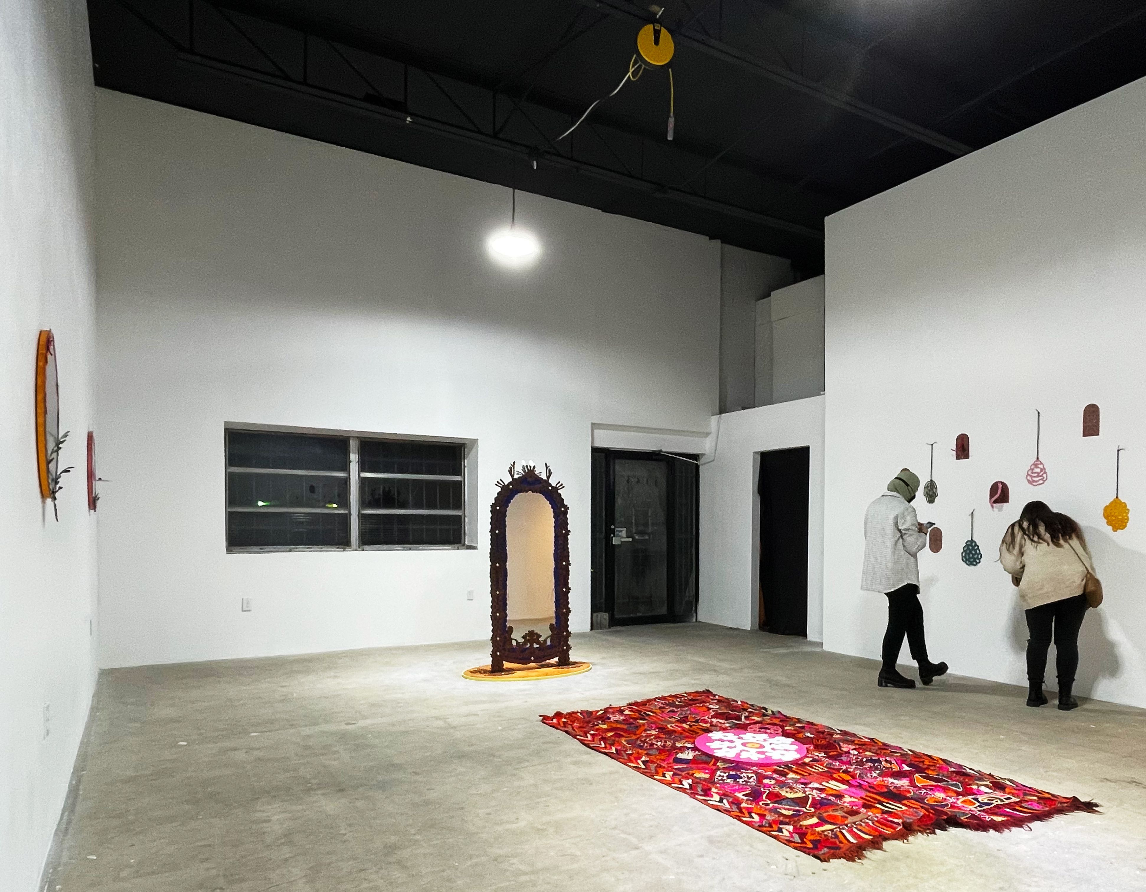 Two visitors observe colorful, varied artworks in a spacious modern gallery with white walls and a concrete floor.