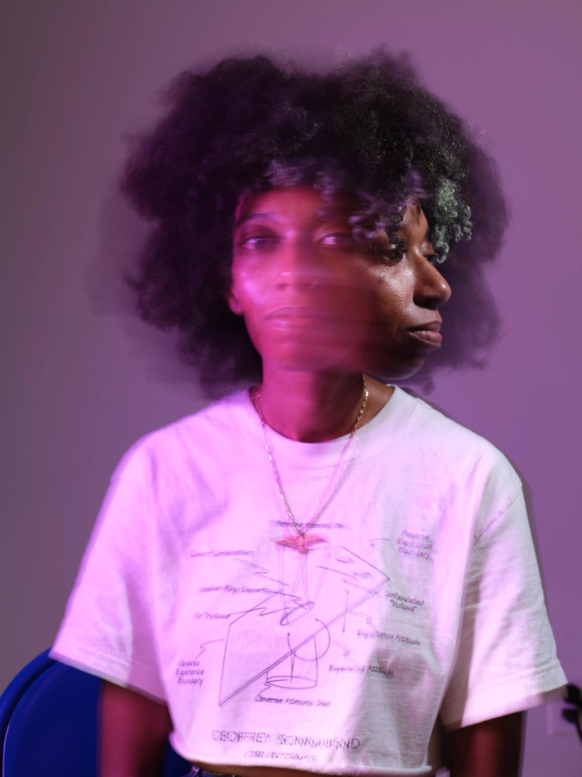 a woman with curly hair is wearing a white t-shirt and a necklace .