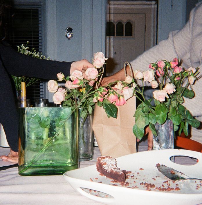 Two people arranging pink roses in vases on a table, with a partially eaten cake on a white plate.