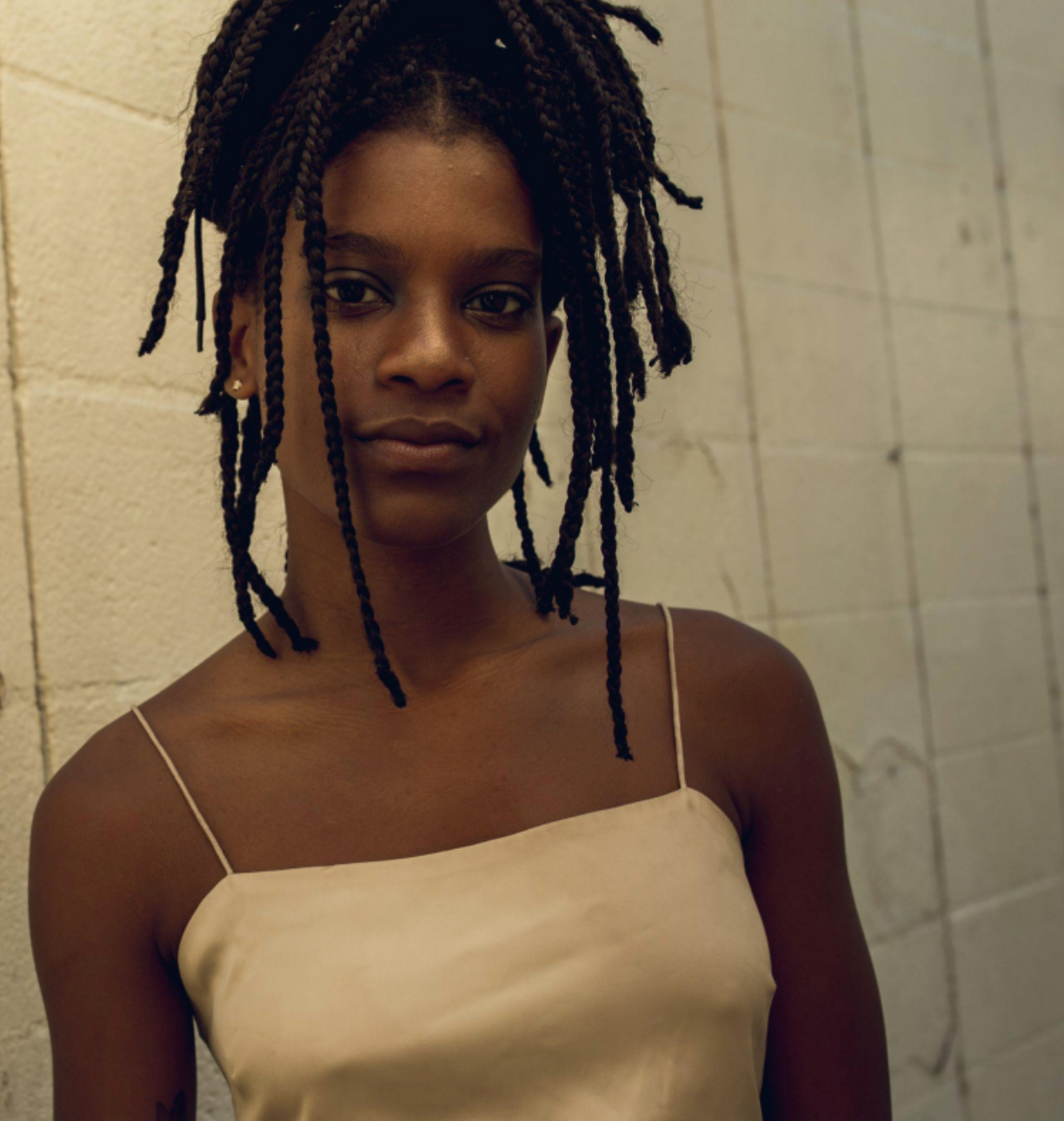 a woman with dreadlocks is wearing a tan tank top