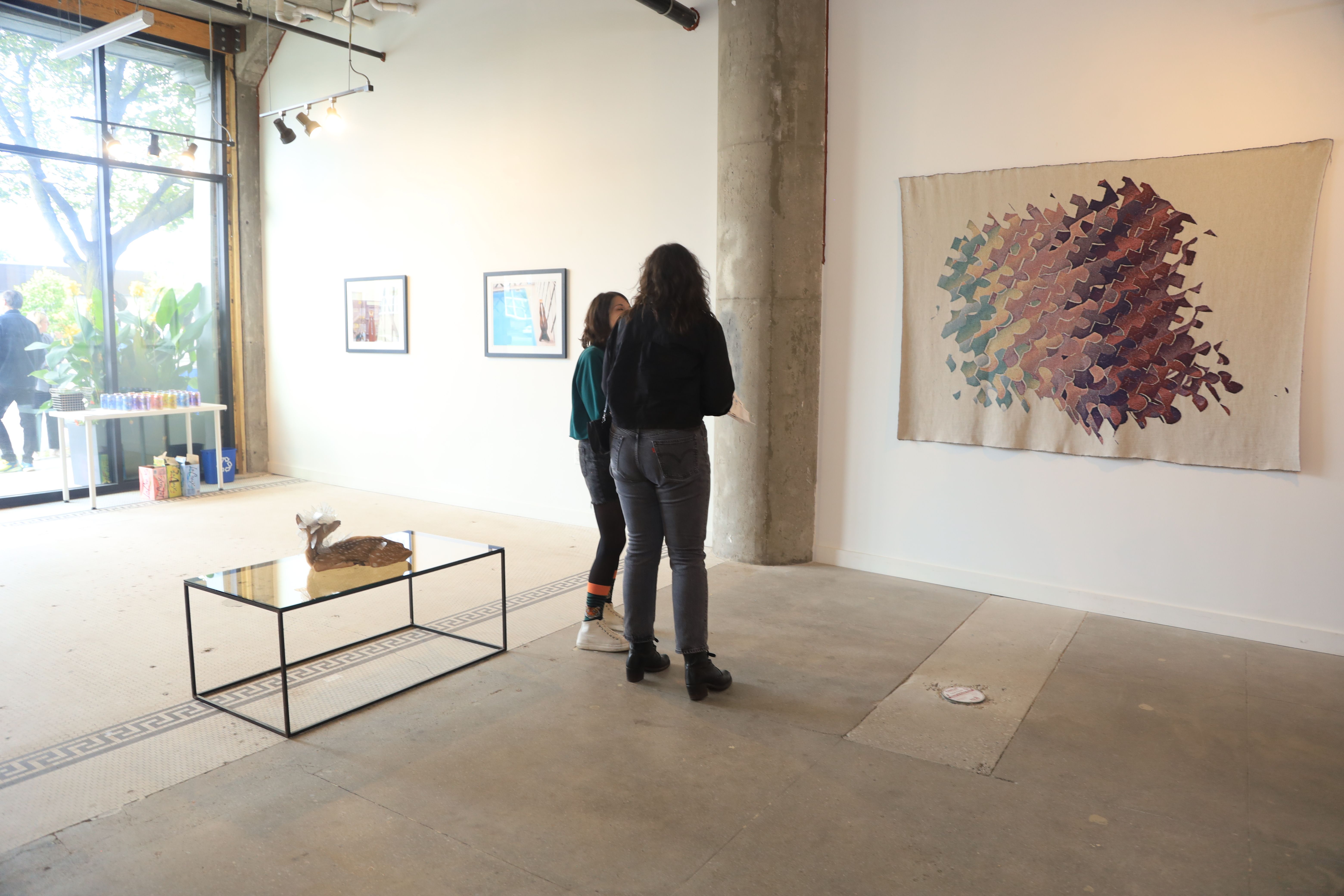 two women are standing in a room looking at a painting .