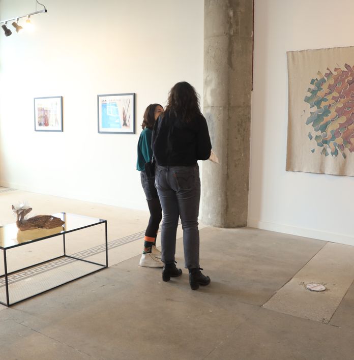 two women are standing in a room looking at a painting .