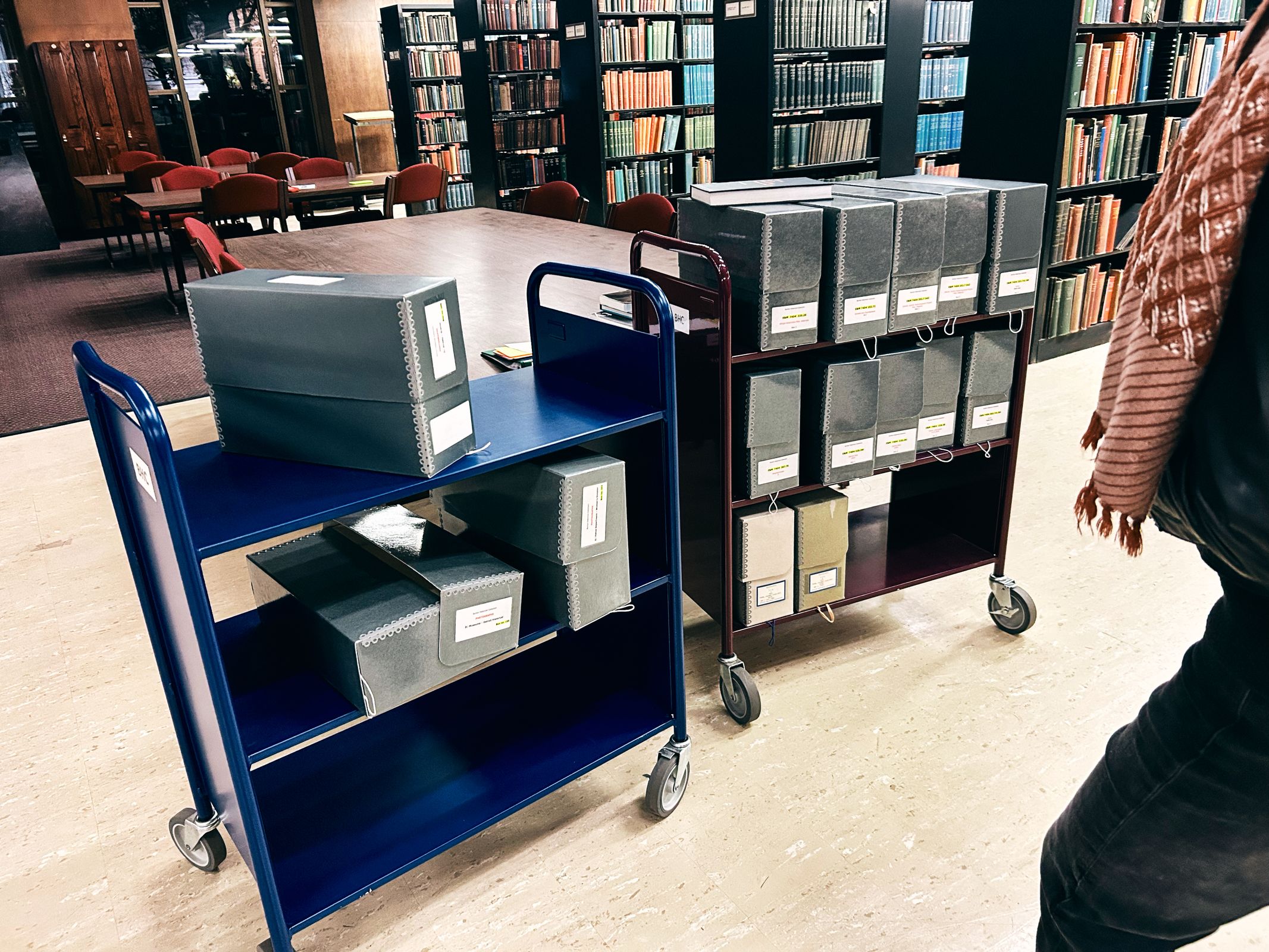 a person is standing next to a cart filled with boxes in a library .