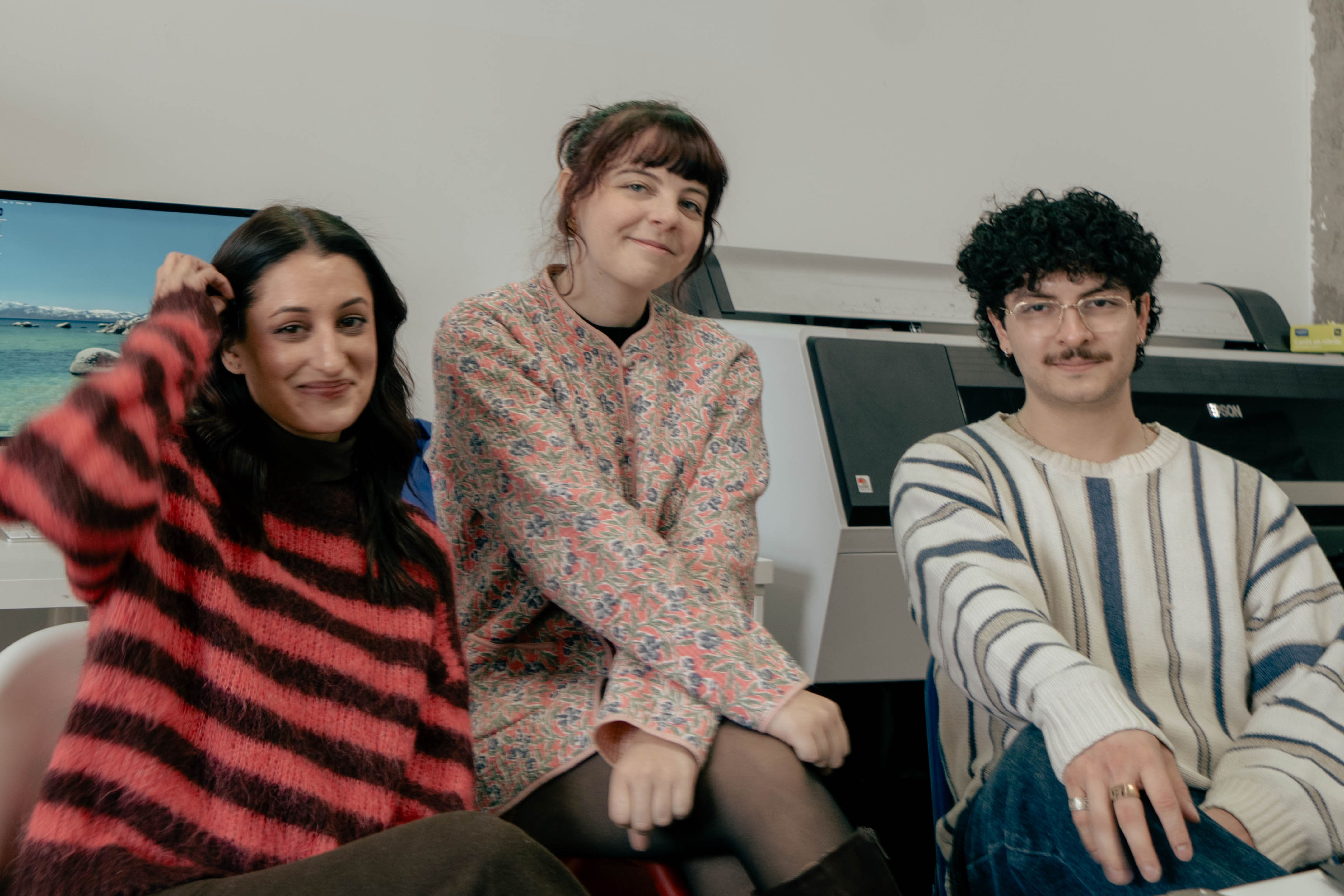 Three smiling people sit in a bright office with "GD 101 WE'RE GLAD YOU'RE HERE" projected on the wall.