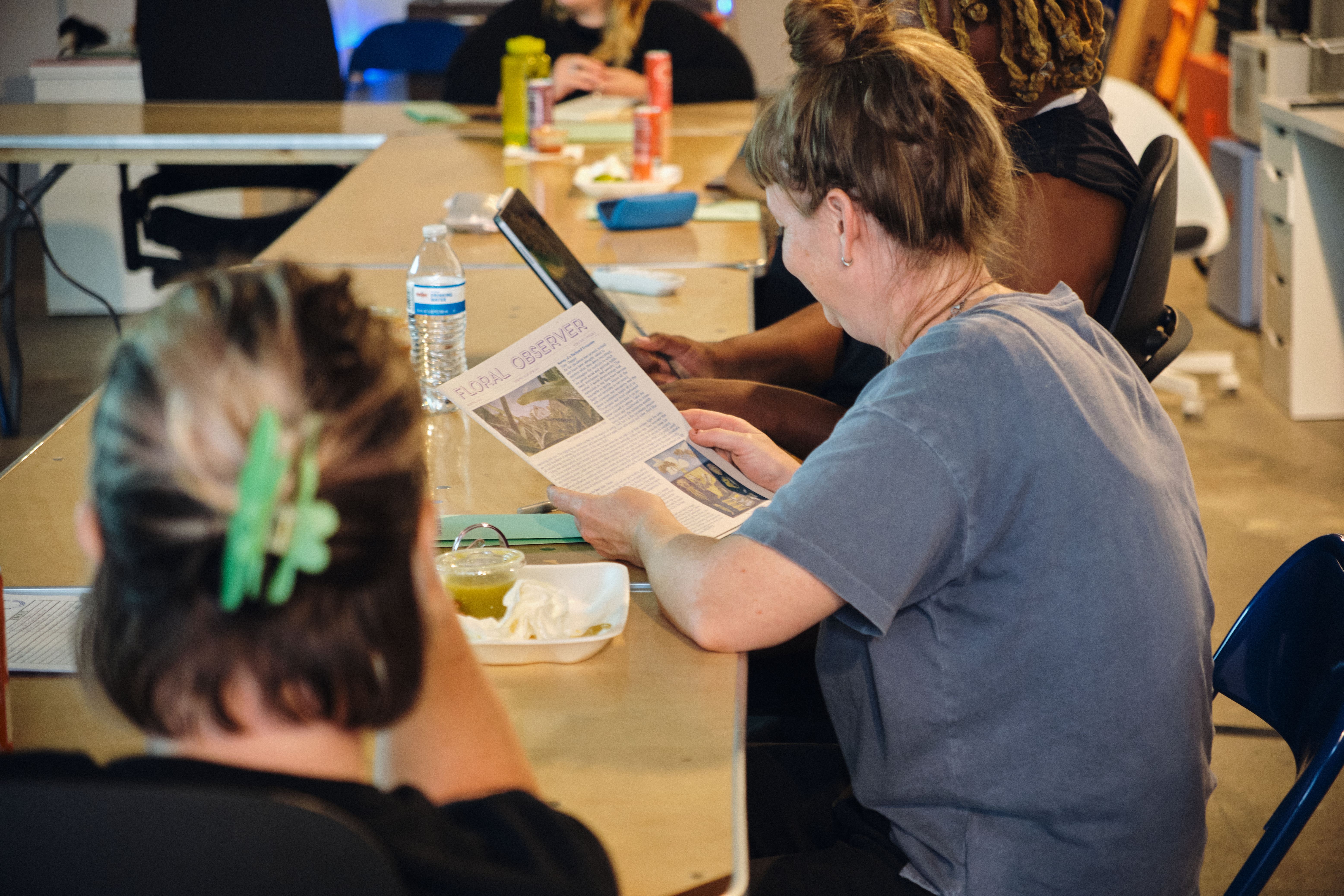 a group of people are sitting at a table reading a newspaper .