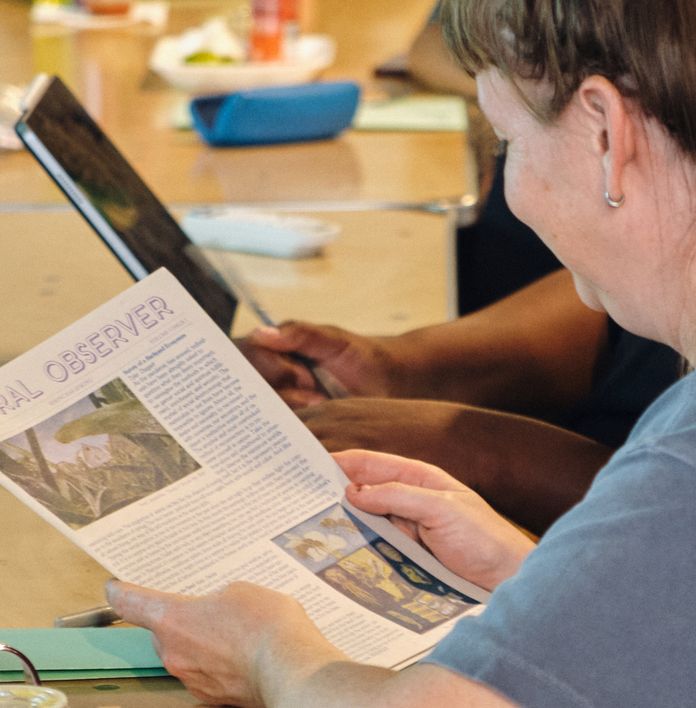 a group of people are sitting at a table reading a newspaper .