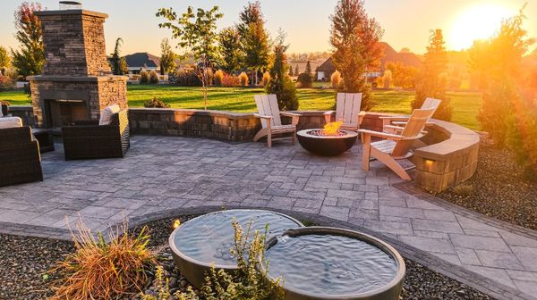 Paver patio in Caldwell, Idaho, with a stone fireplace, fire pit, and Aquascape fountain in morning light