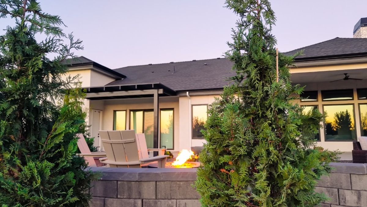 Evening view from the stone wall toward the house, with the fire pit lit between arborvitae