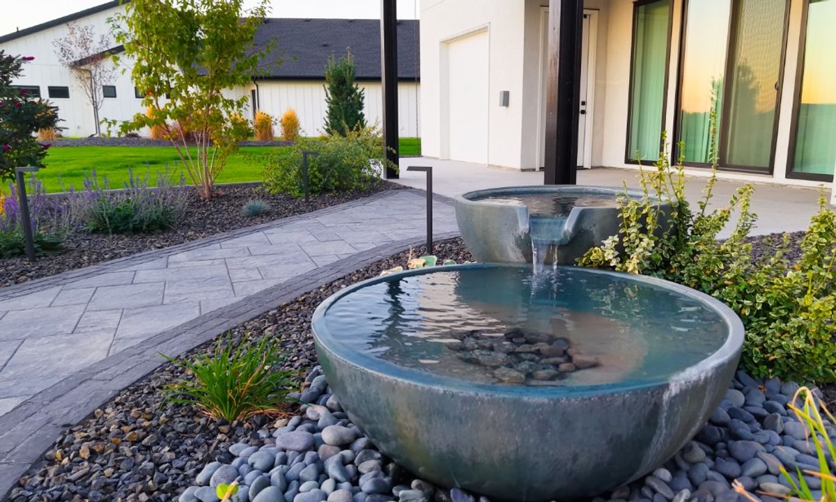 Two-bowl Aquascape fountain spilling into a river-rock bed beside the walkway