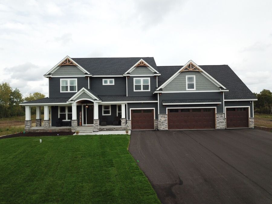 Two-story home with dark horizontal siding, gray shake-style gable accents, white trim, and stone details.
