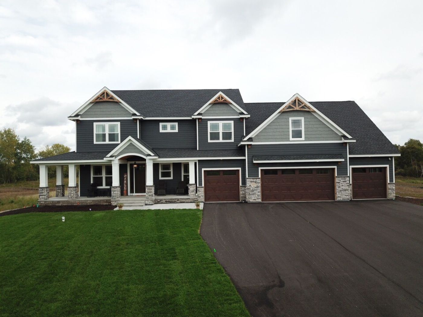 Two-story home with dark horizontal siding, gray shake-style gable accents, white trim, and stone details.