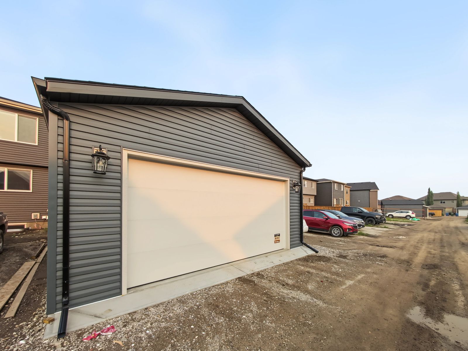 The garage from along the gravel lane, showing the overhead door, a lantern, the downspout and the concrete apron