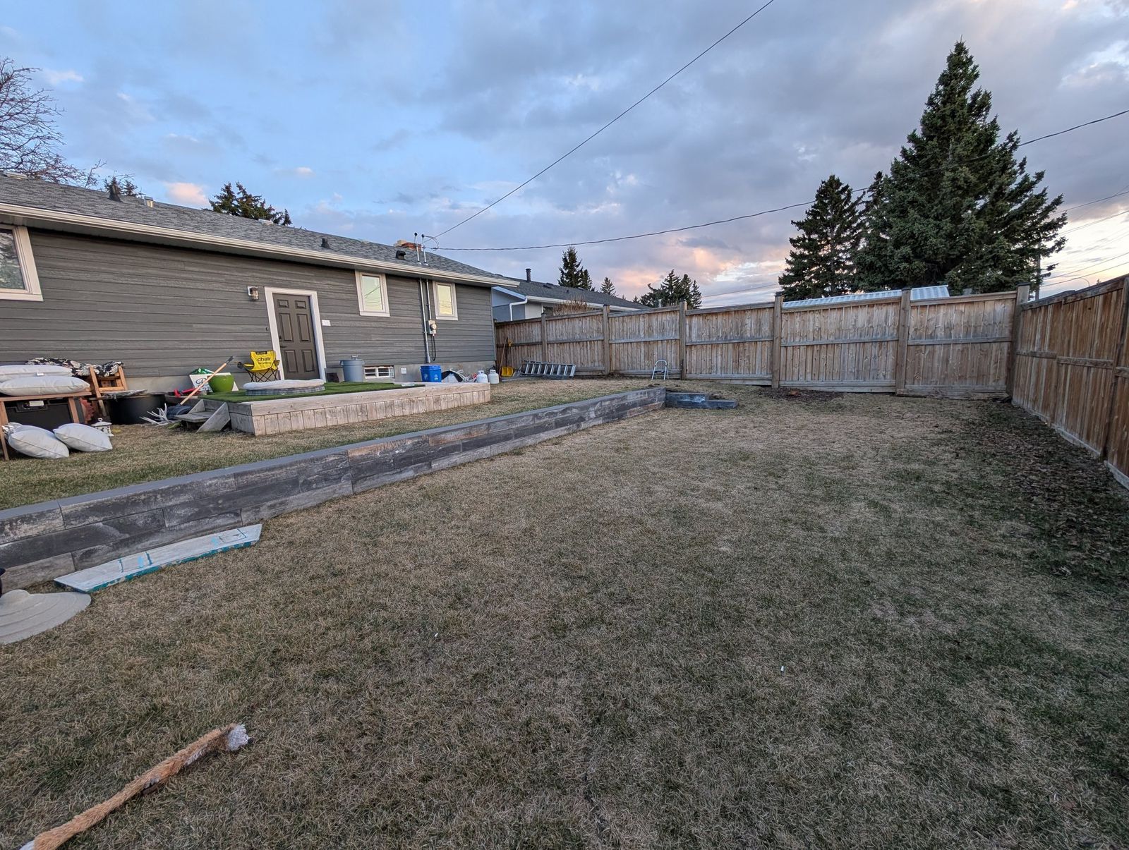 The back yard before the build: grass to the fence, with an overhead line running from the house across the yard