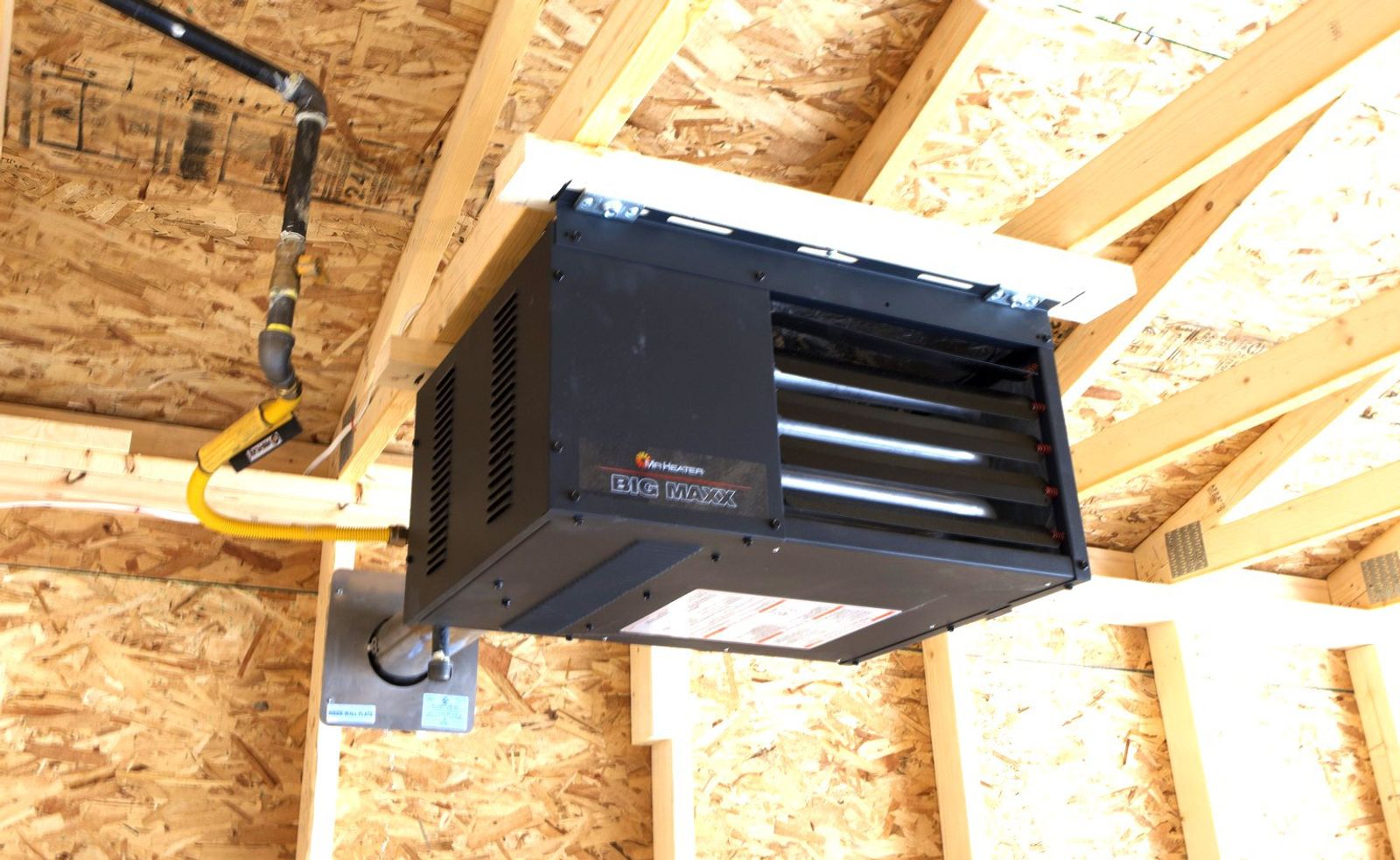 Gas unit heater hung from the ceiling framing, with the black gas line, shut-off valve and yellow flexible connector running to it
