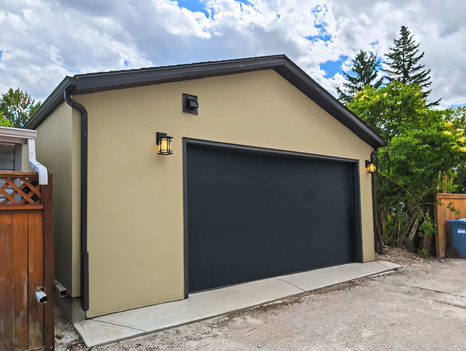 The garage from the far side of the lane, showing the stucco return, brown fascia and the downspout