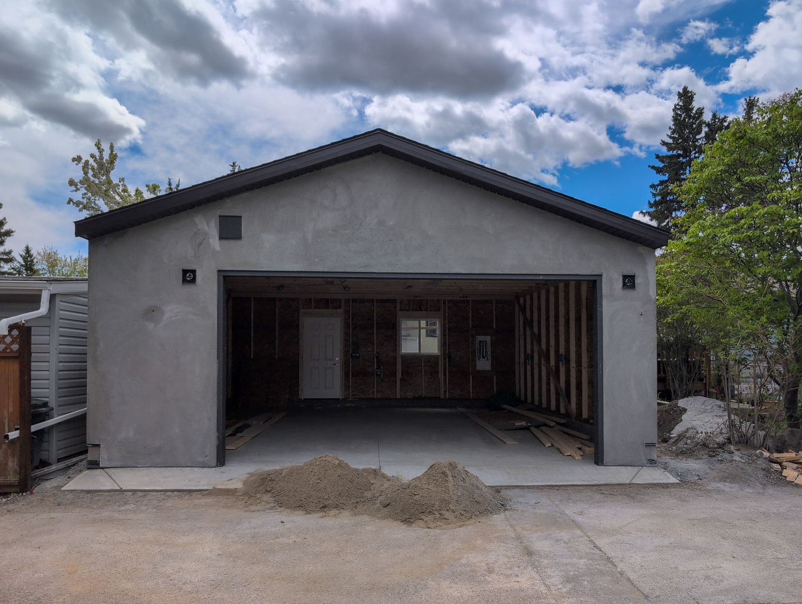 The garage part way through: grey stucco base coat on, the overhead door not yet hung, framing visible inside
