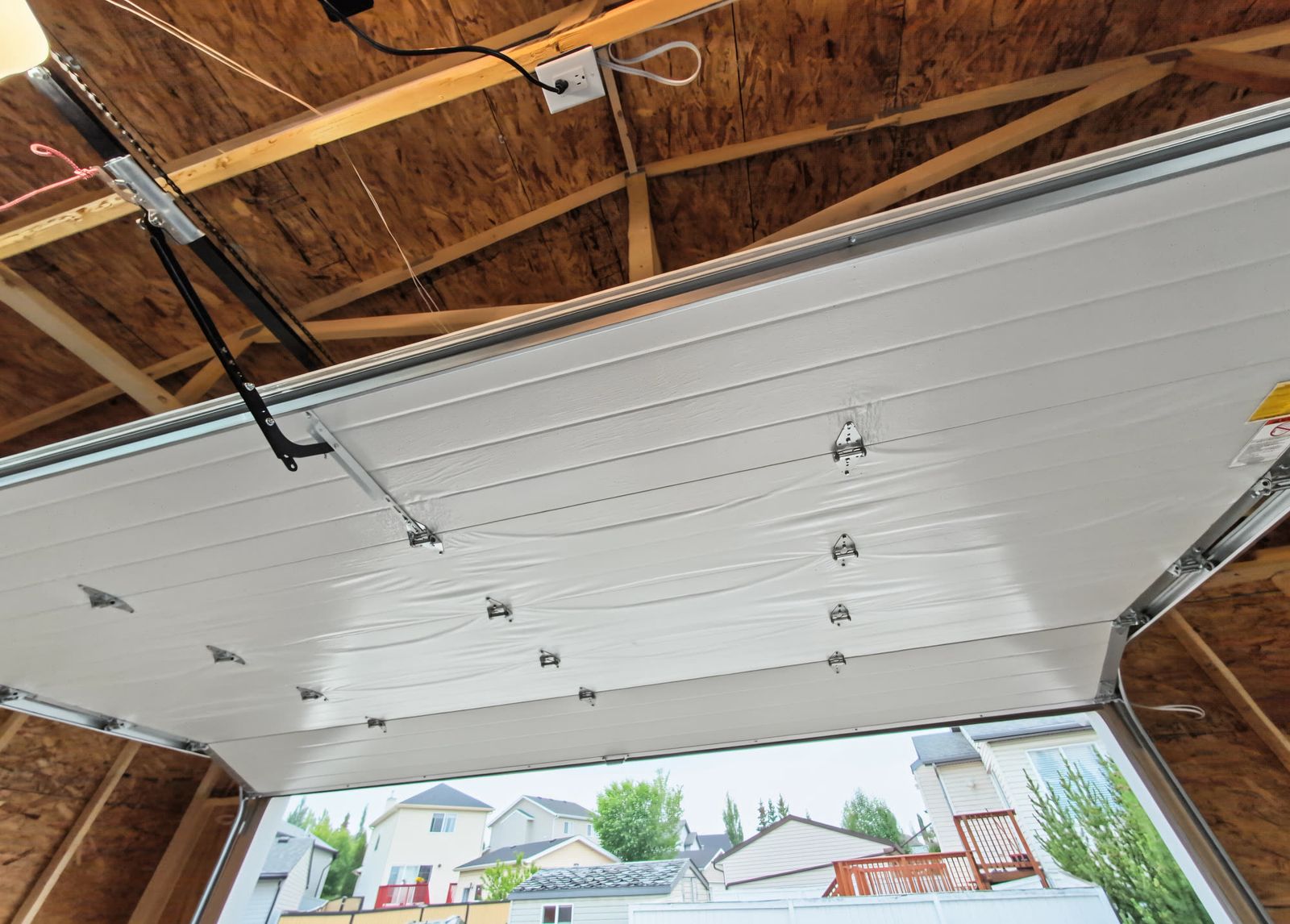 Looking up from inside at the overhead door open flat on its ceiling tracks, with the trusses and sheathing above it