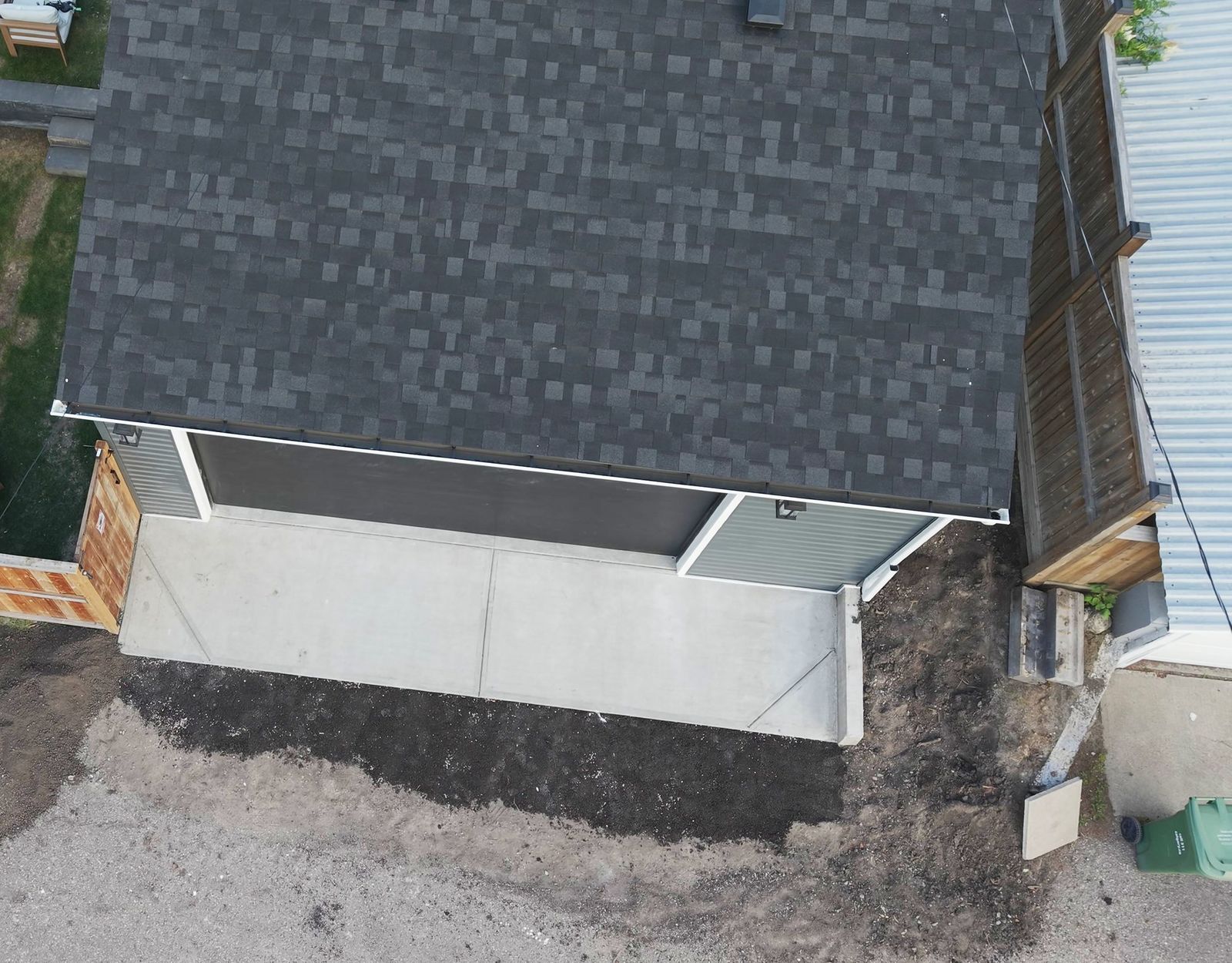 The garage from above: dark shingled roof, the concrete apron sloping down to the lane and the concrete retaining wall along its edge