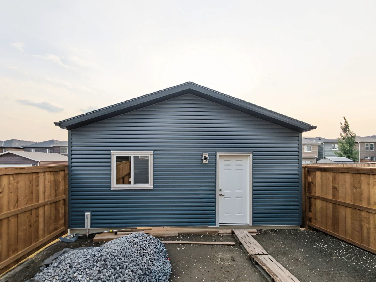 The back of the garage from the yard: a sliding window, a white man door with a motion light beside it, and new cedar fence each side