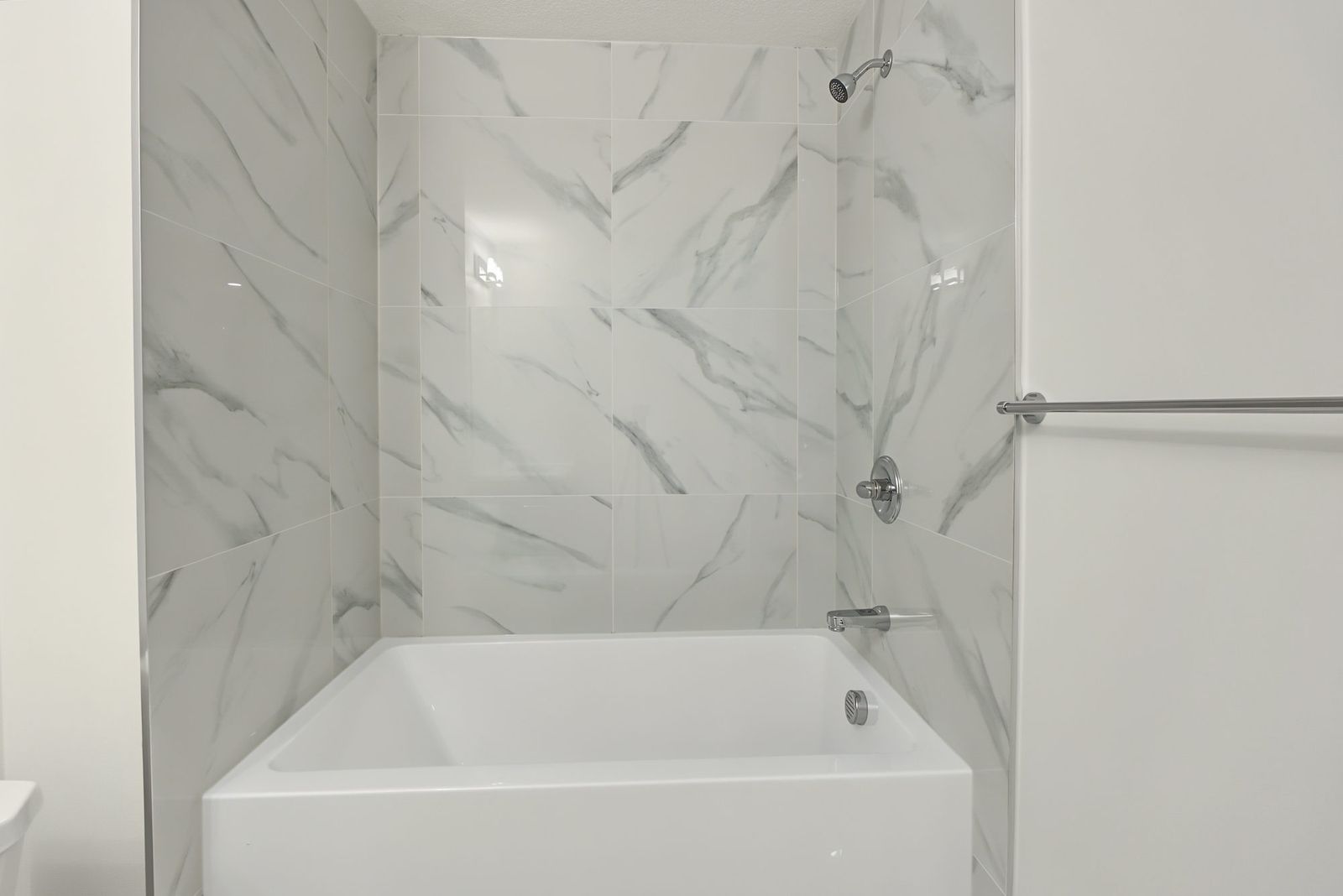 Alcove tub with marble-look tile to the ceiling and a chrome shower set