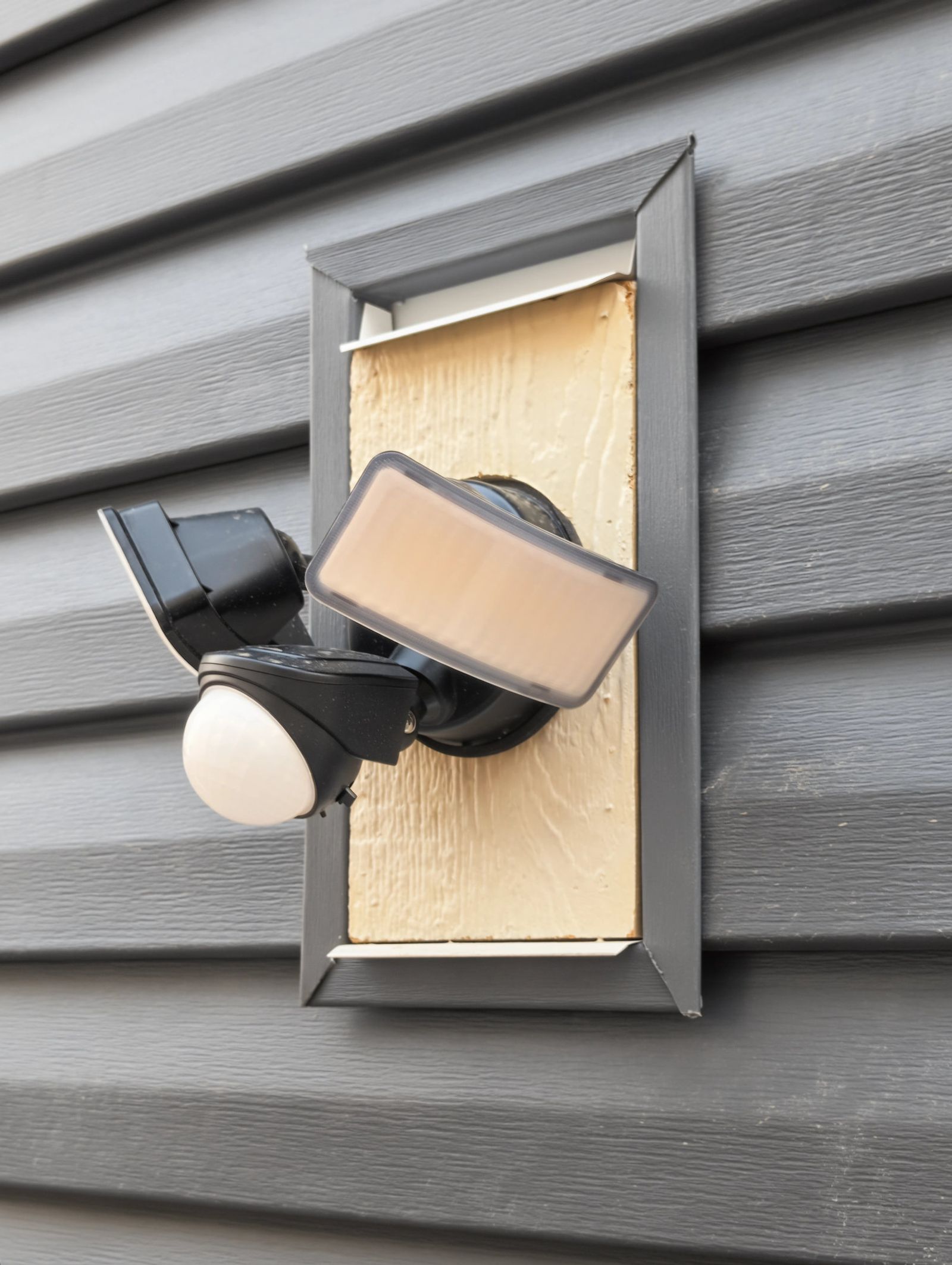 The twin-head motion flood light on its siding mounting block