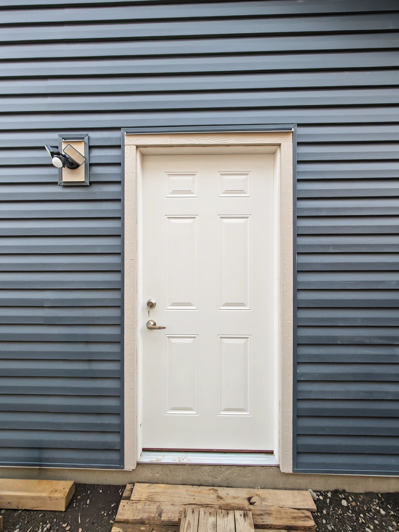 The white six-panel man door in white trim with the motion flood light mounted beside it