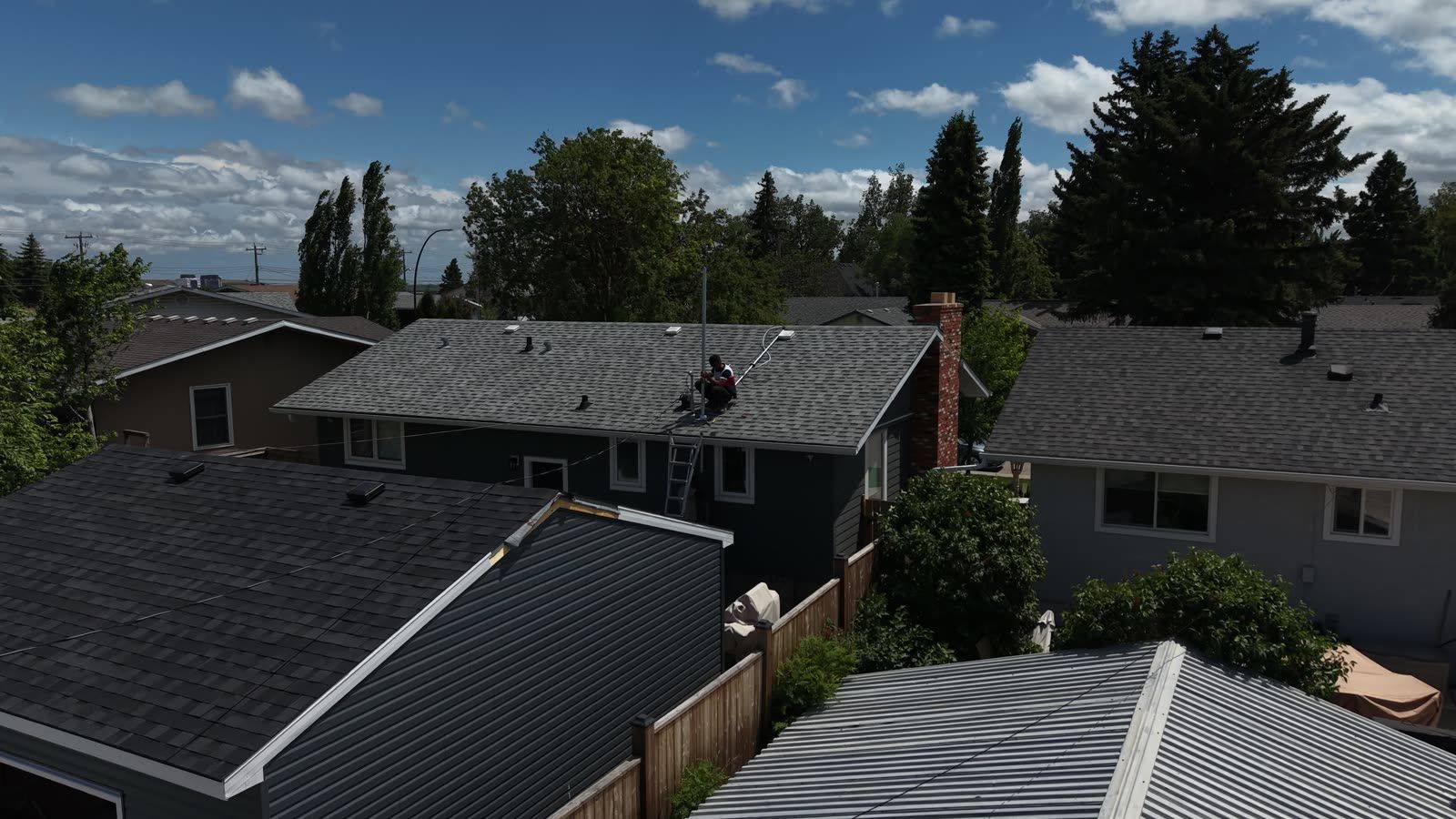 Aerial view of an electrician on the house roof working at the service mast where the overhead lines land, with the new garage below