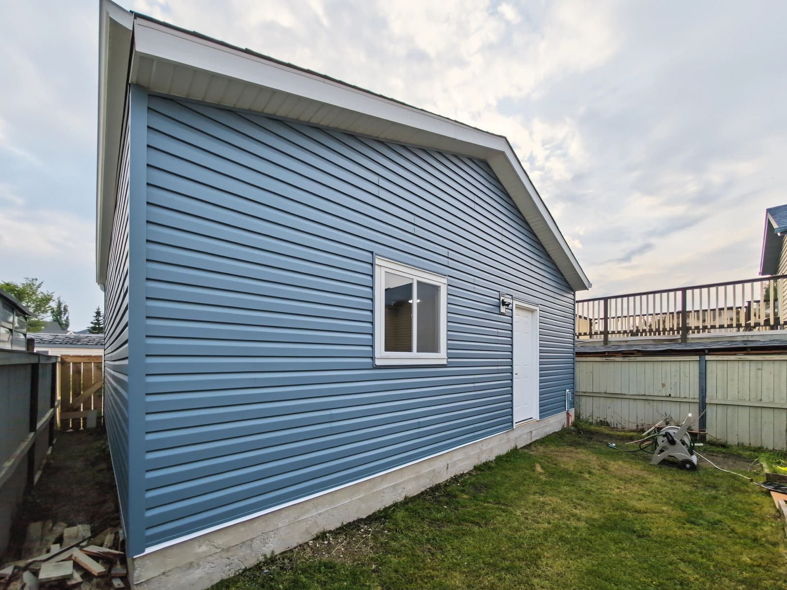 The garage from the back corner of the yard, showing the long side wall, the window and the roof line against the evening sky