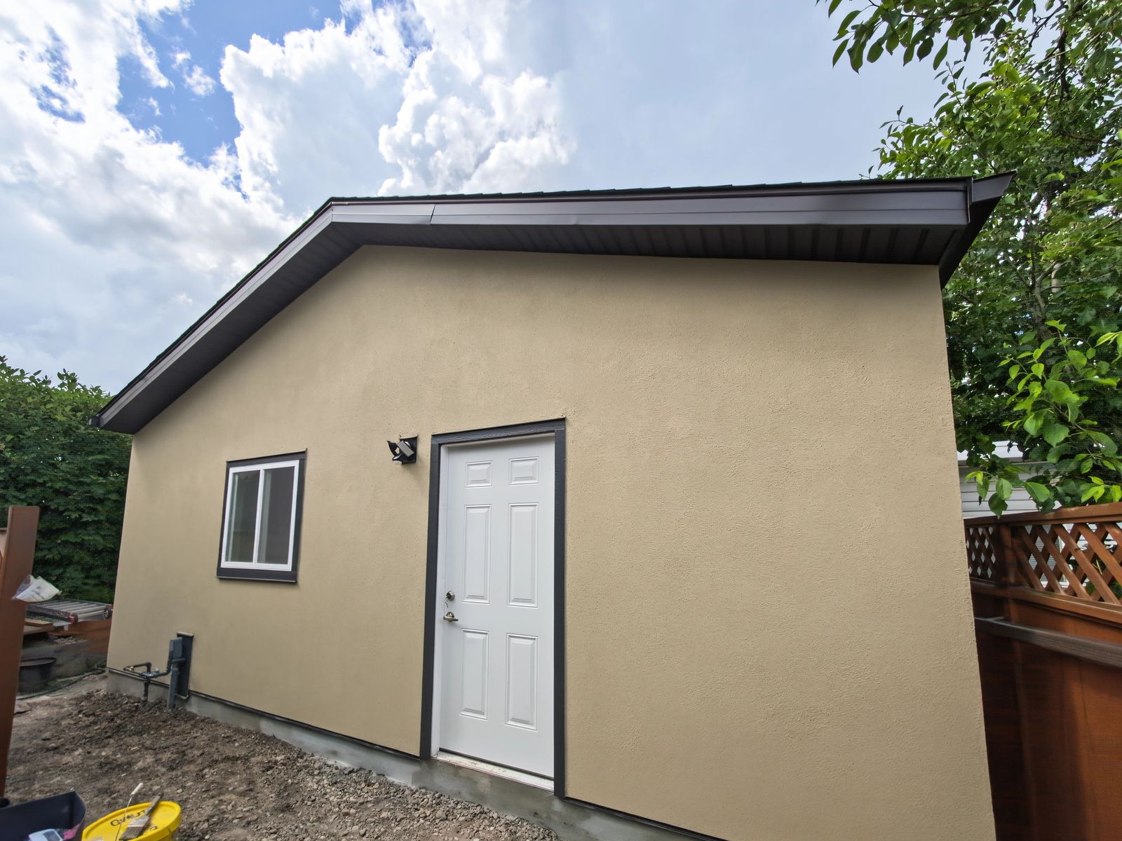 Stucco side wall with a white man door in black trim and a sliding window
