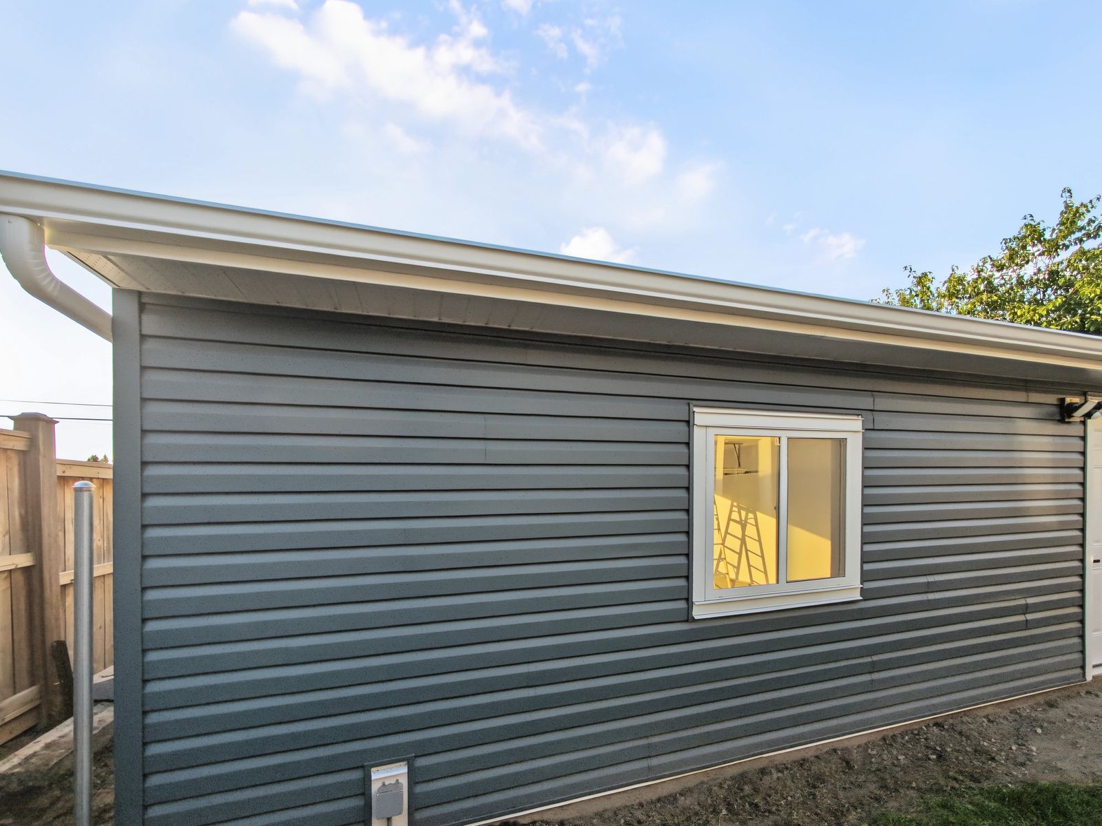 Close view of the dark grey vinyl lap siding, the white-trimmed sliding window and the aluminium soffit and eavestrough above