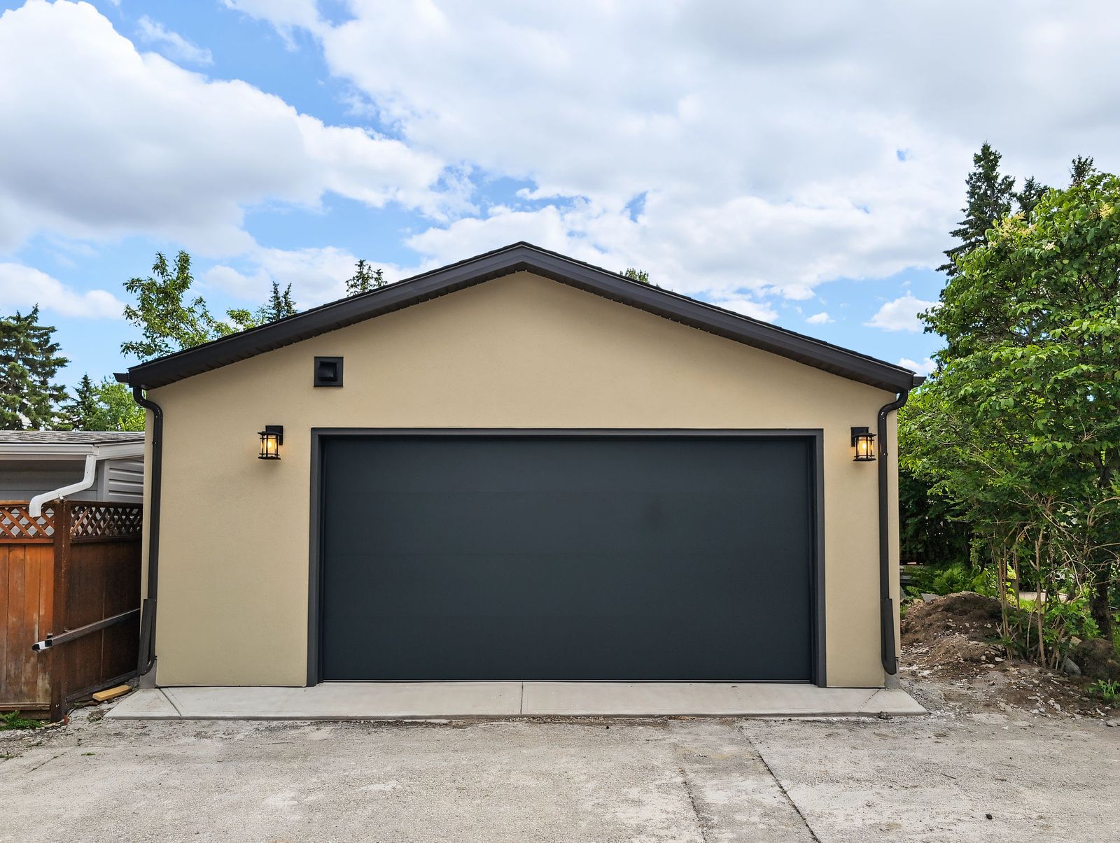 The finished garage straight on from the lane: black 16 by 8 overhead door in a tan stucco wall, lantern each side