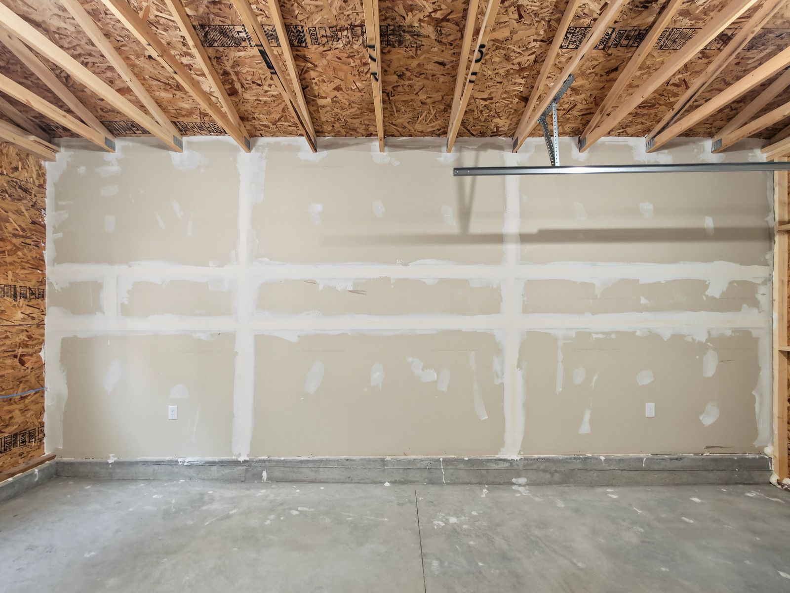 The fire-rated drywall wall straight on, joints and screw heads taped, with the door track and open trusses above