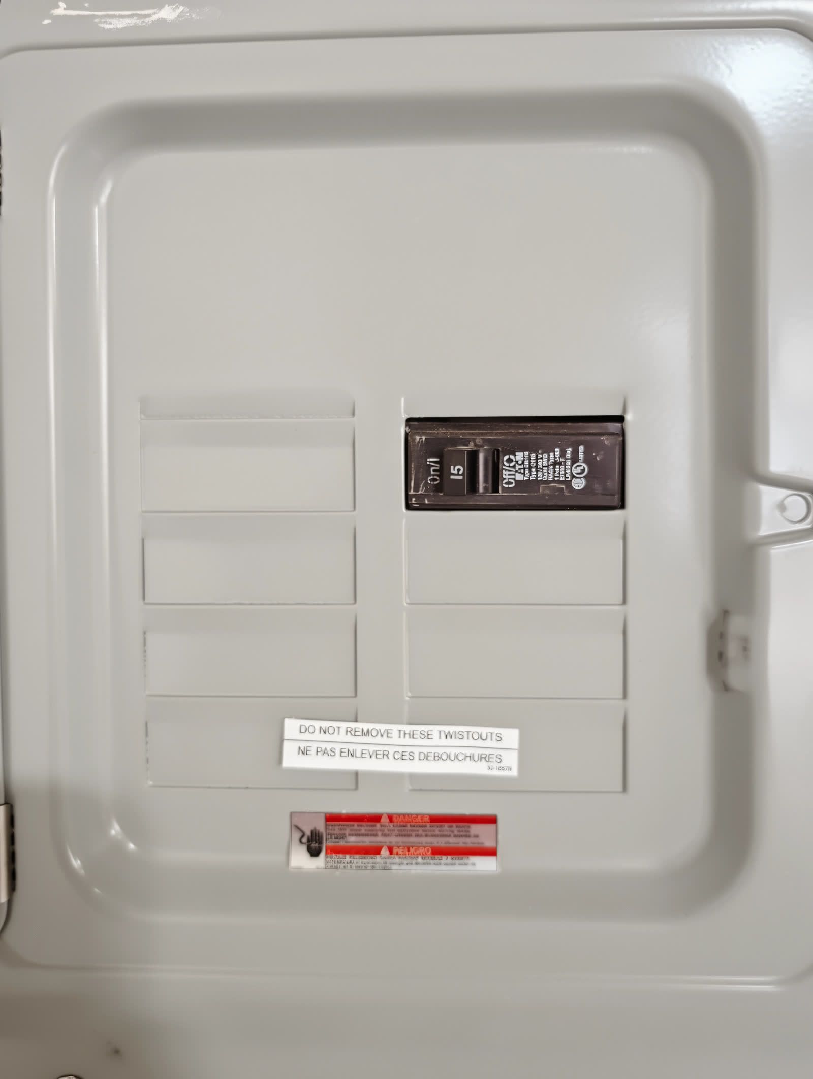 The inside of the sub panel cover with one breaker in place and the unused twistouts still closed