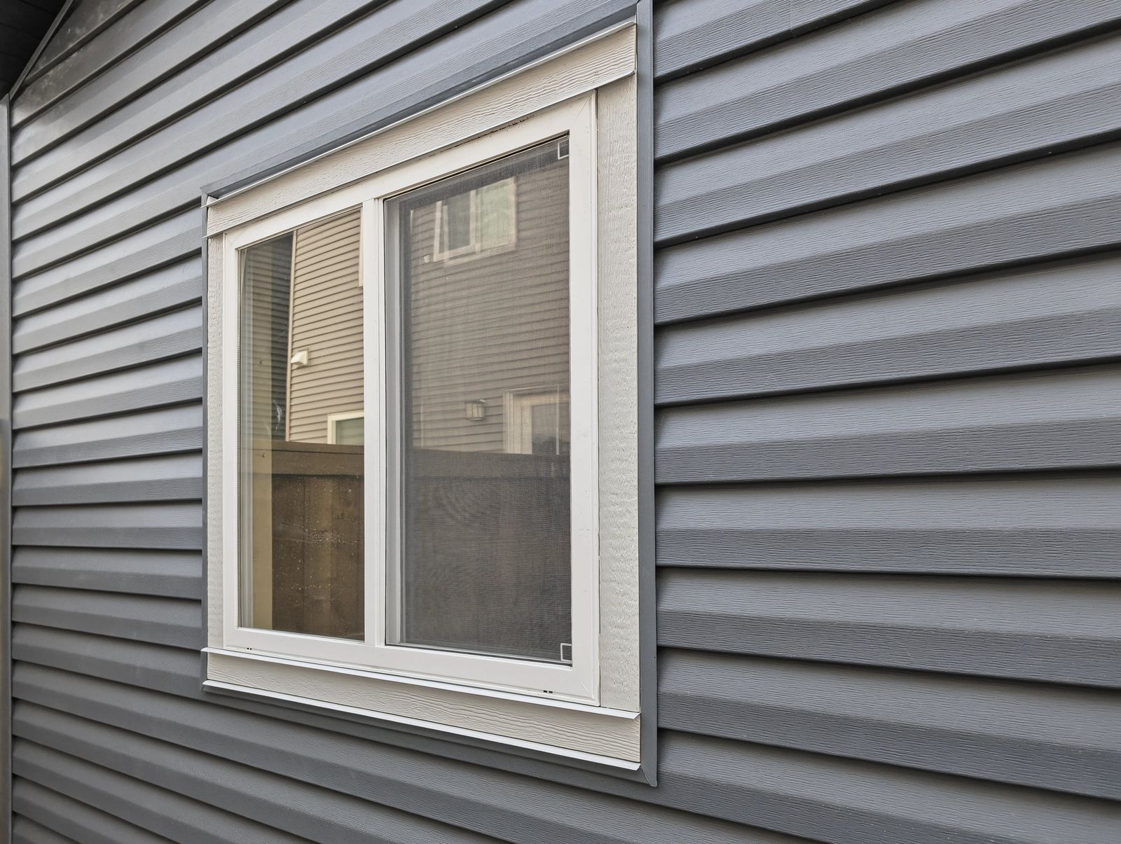 Close view of the sliding window in its textured white trim against the dark lap siding