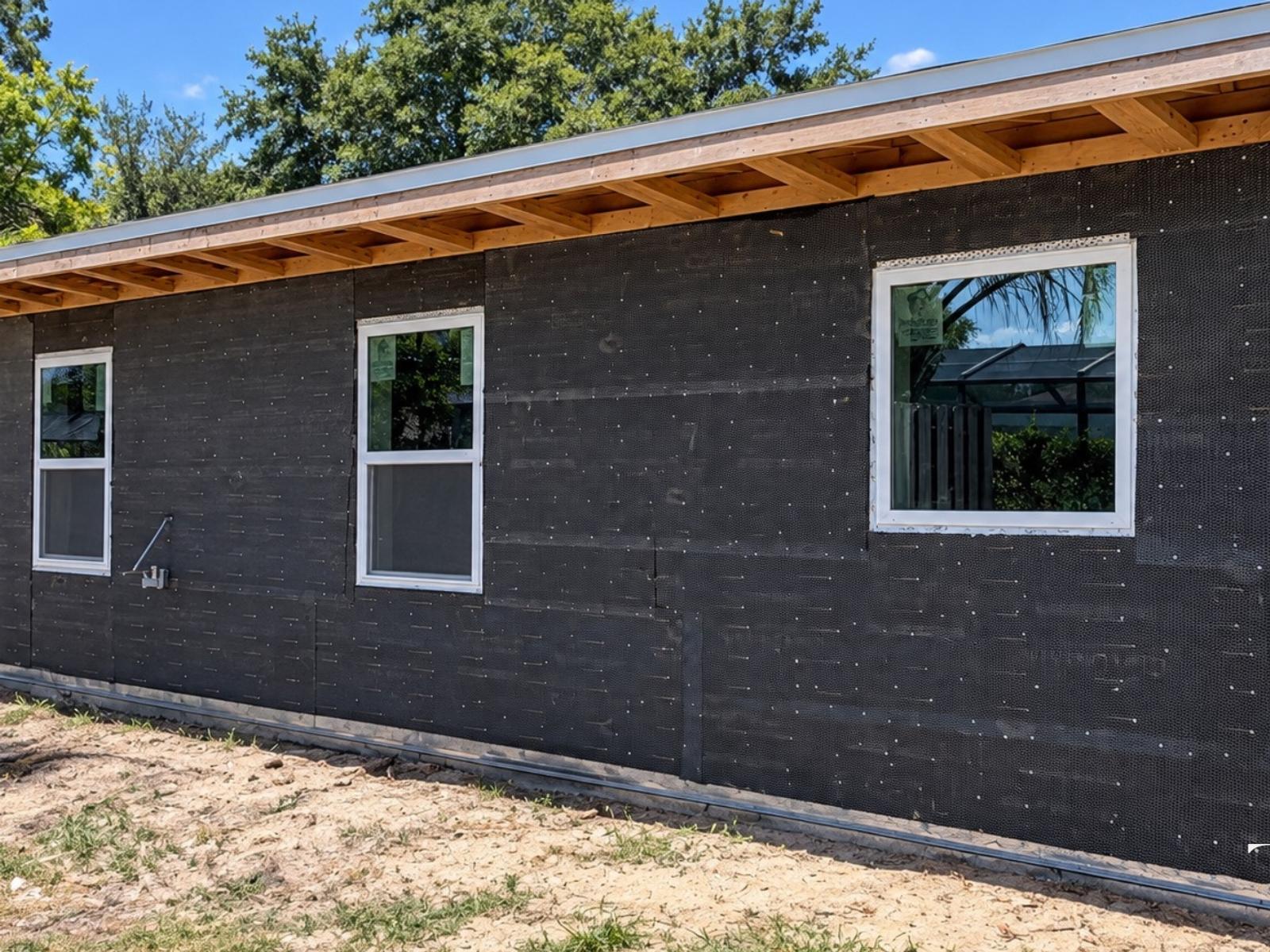 Home addition during construction with wall wrap, installed windows and exposed roof framing