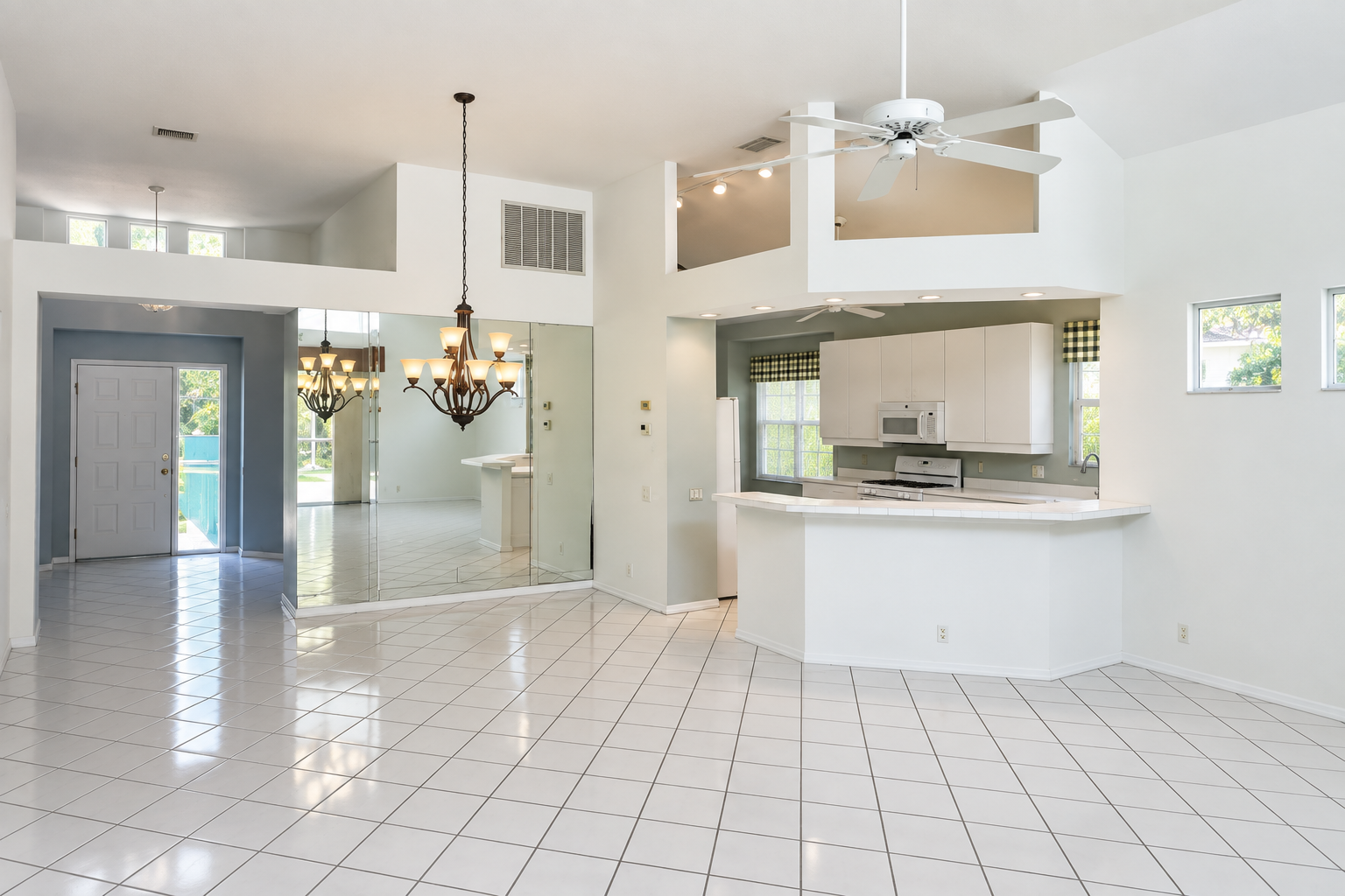 Sarasota kitchen before remodeling, with a raised peninsula, white cabinets, mirrored wall and square tile floor.