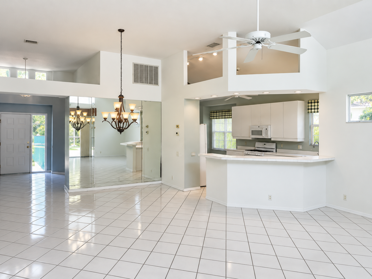 Sarasota kitchen before remodeling, with a raised peninsula, white cabinets, mirrored wall and square tile floor.
