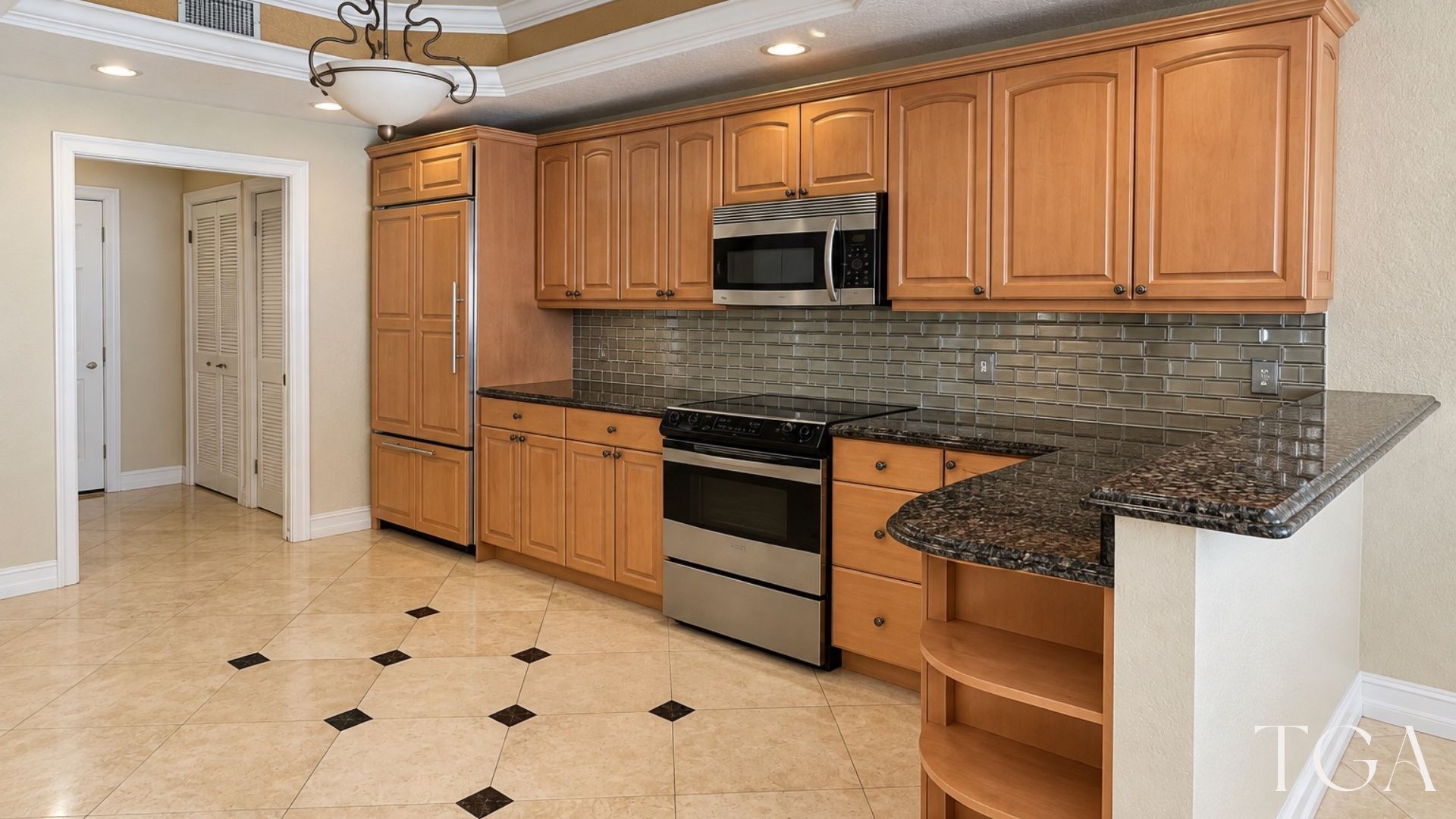 Before remodeling: brown kitchen cabinets, dark counters, a tile backsplash and curved open shelves at the counter end