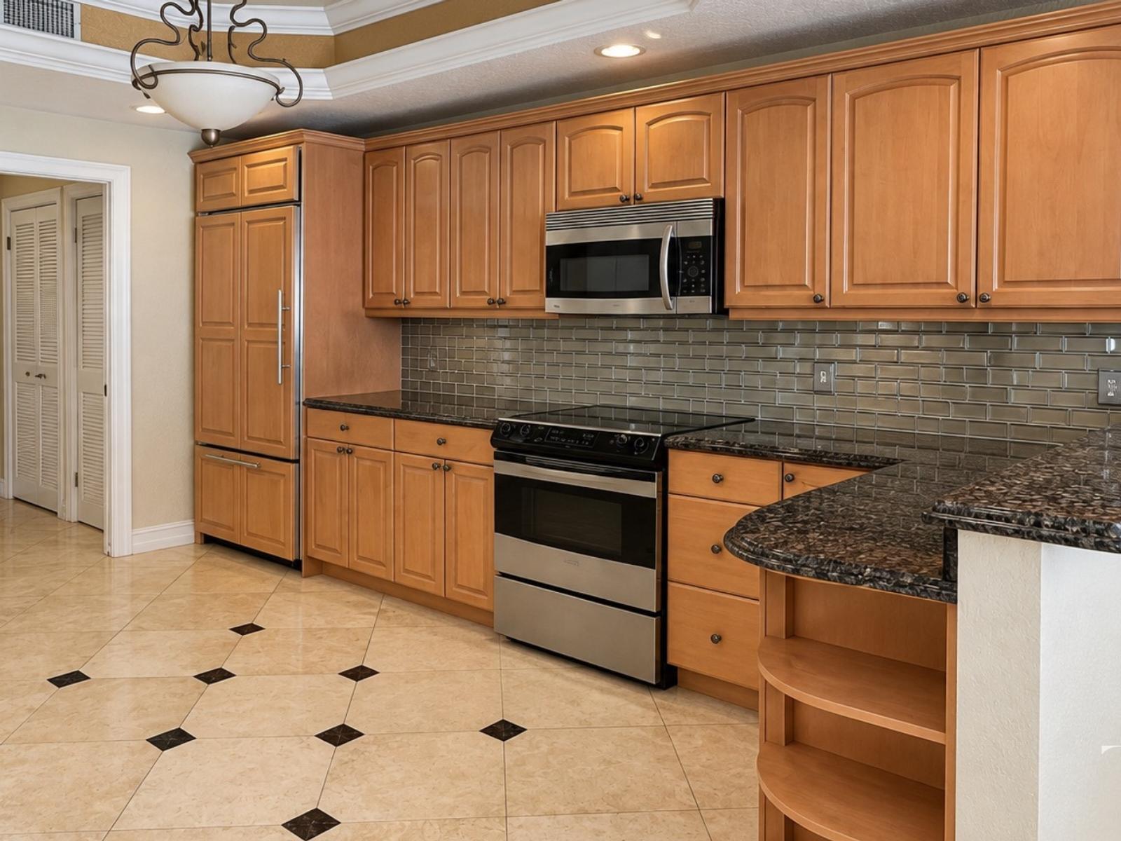 Before remodeling: brown kitchen cabinets, dark counters, a tile backsplash and curved open shelves at the counter end