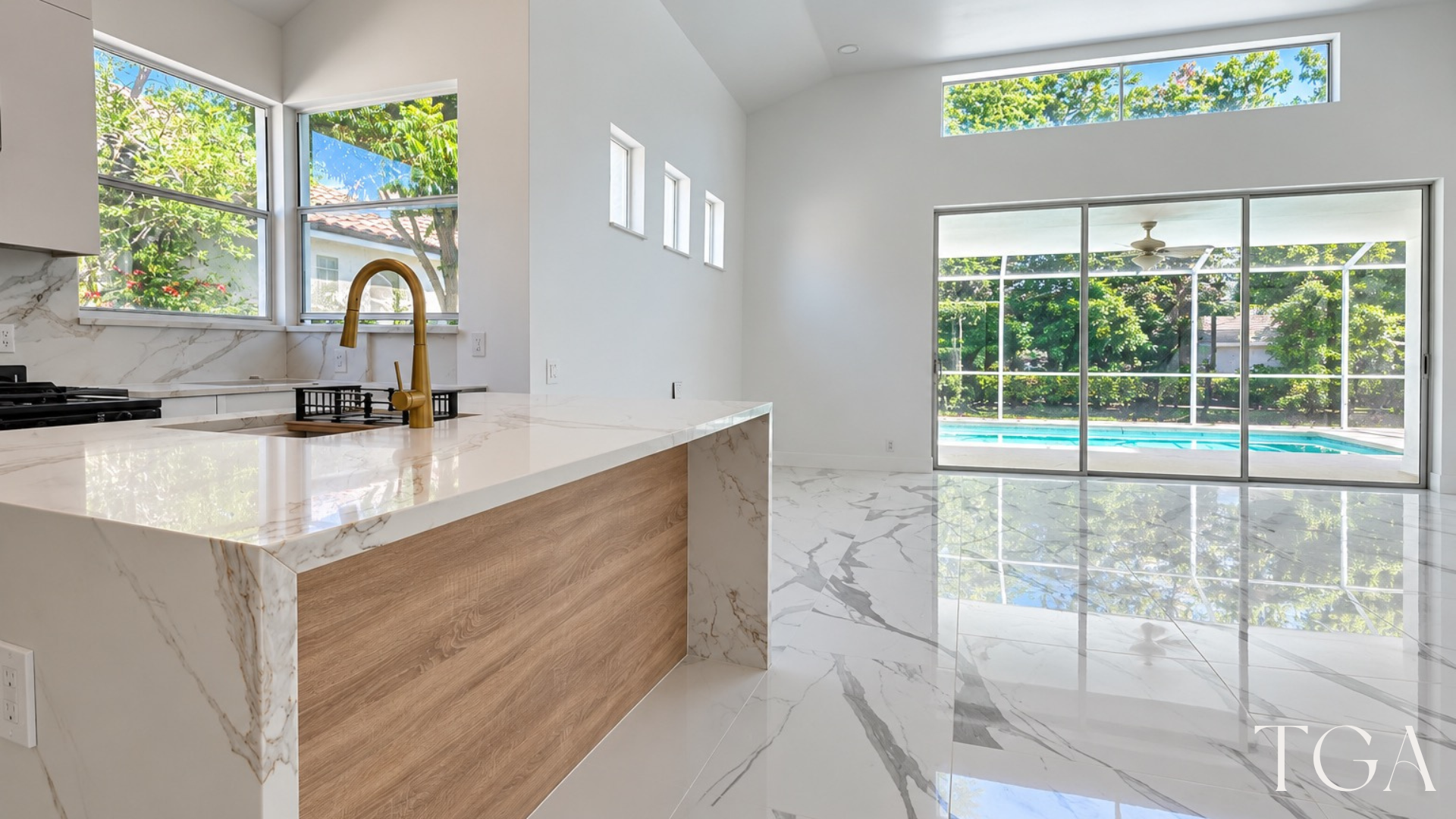 Waterfall kitchen island beside an open living space with sliding glass doors overlooking a screened pool.