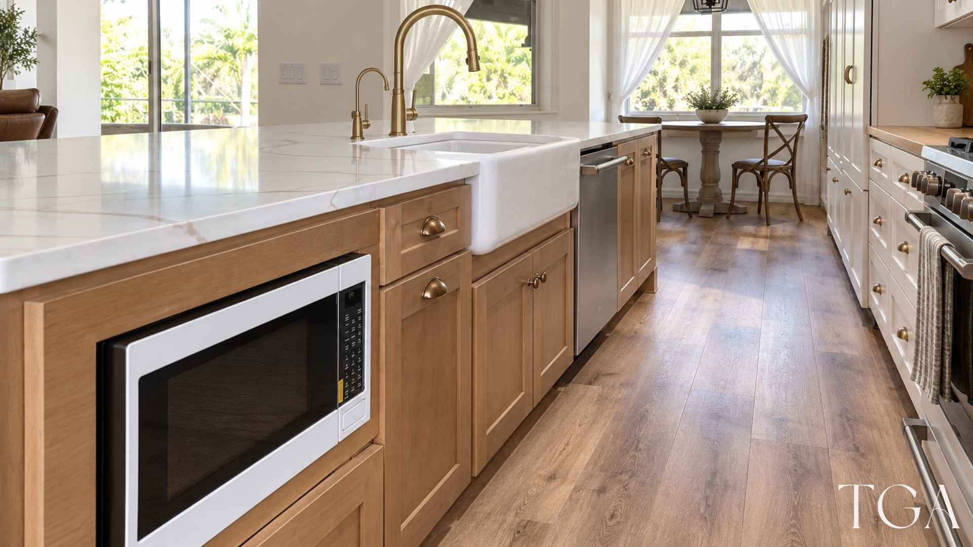 Apron-front kitchen sink with gold-toned faucets, a microwave set into the wood-tone island and a nearby dishwasher.