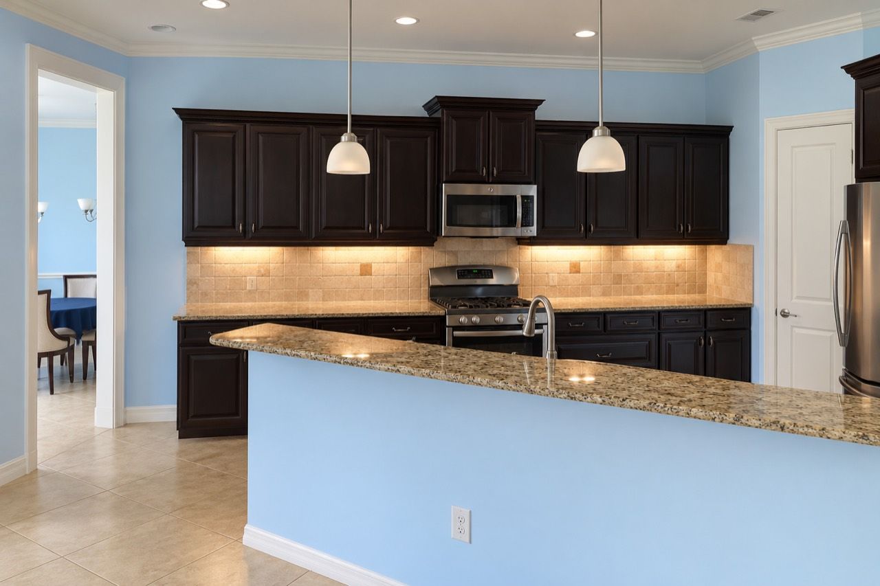 Sarasota kitchen before remodeling, with dark raised-panel cabinets, blue walls, beige tile backsplash and a raised peninsula.