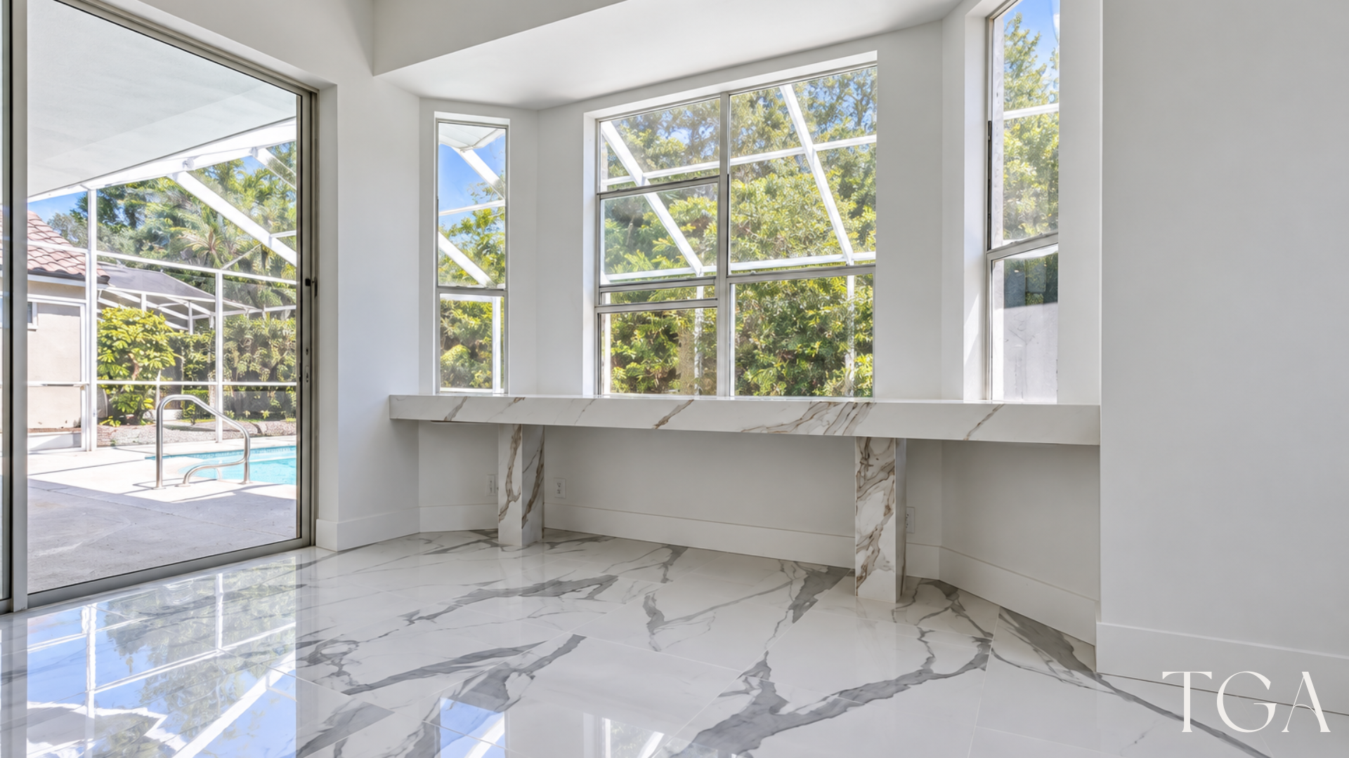 Long built-in counter beneath tall windows beside sliding glass doors and white veined tile flooring.