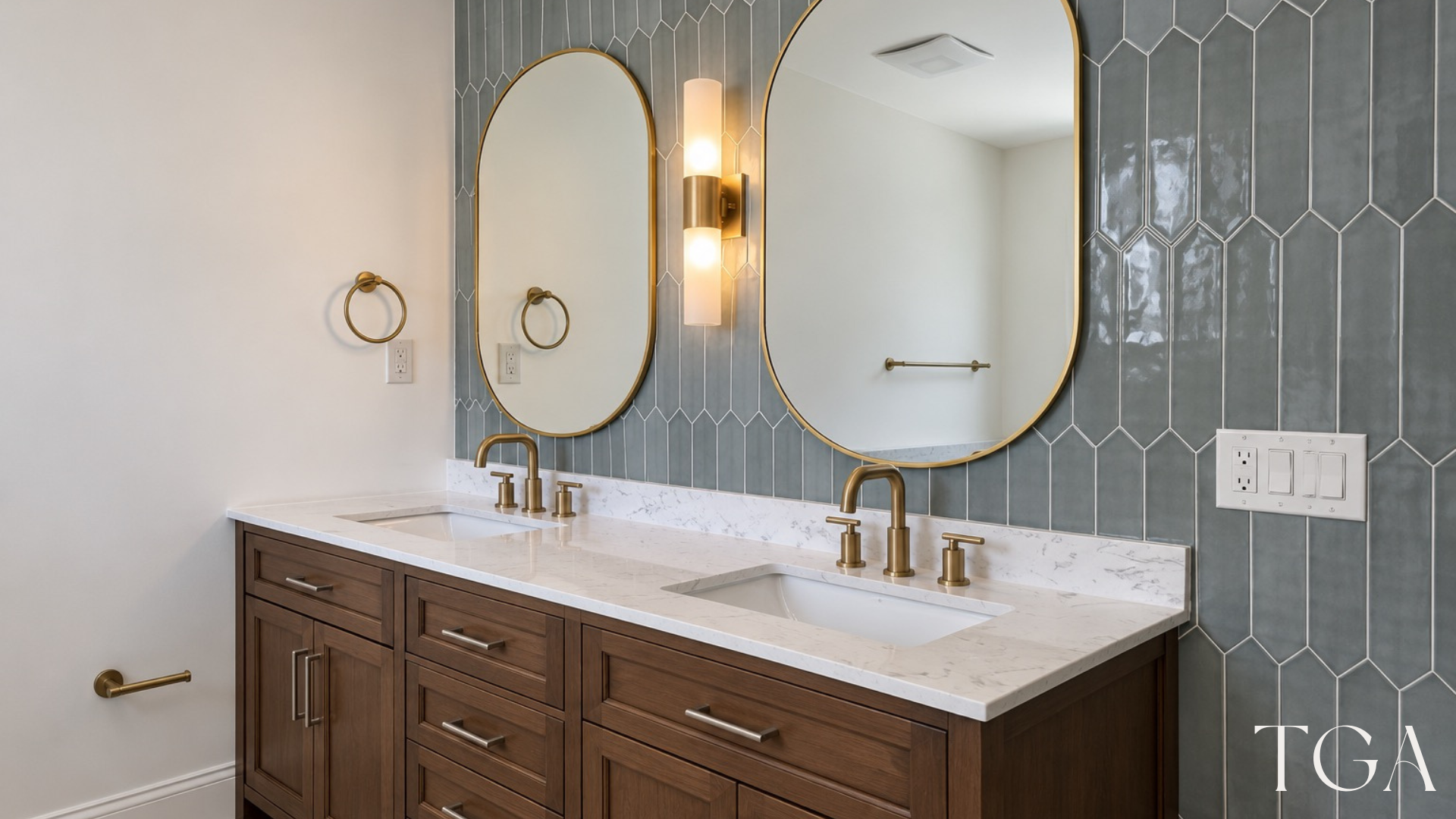 Wood-tone double vanity beneath oval mirrors and wall lights against blue-green accent tile