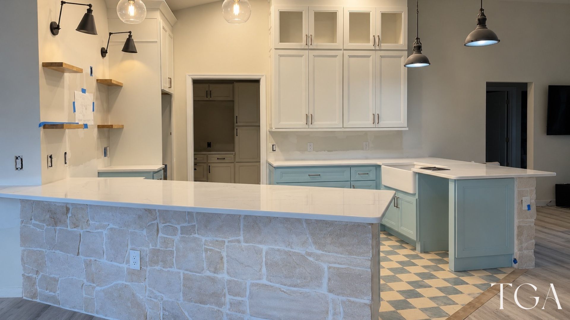 Wide view of the aqua kitchen with a stone-faced counter front, black pendant lights and checkerboard floor