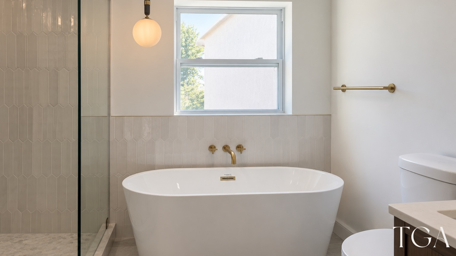White freestanding bathtub beneath a window beside the glass shower and a globe pendant