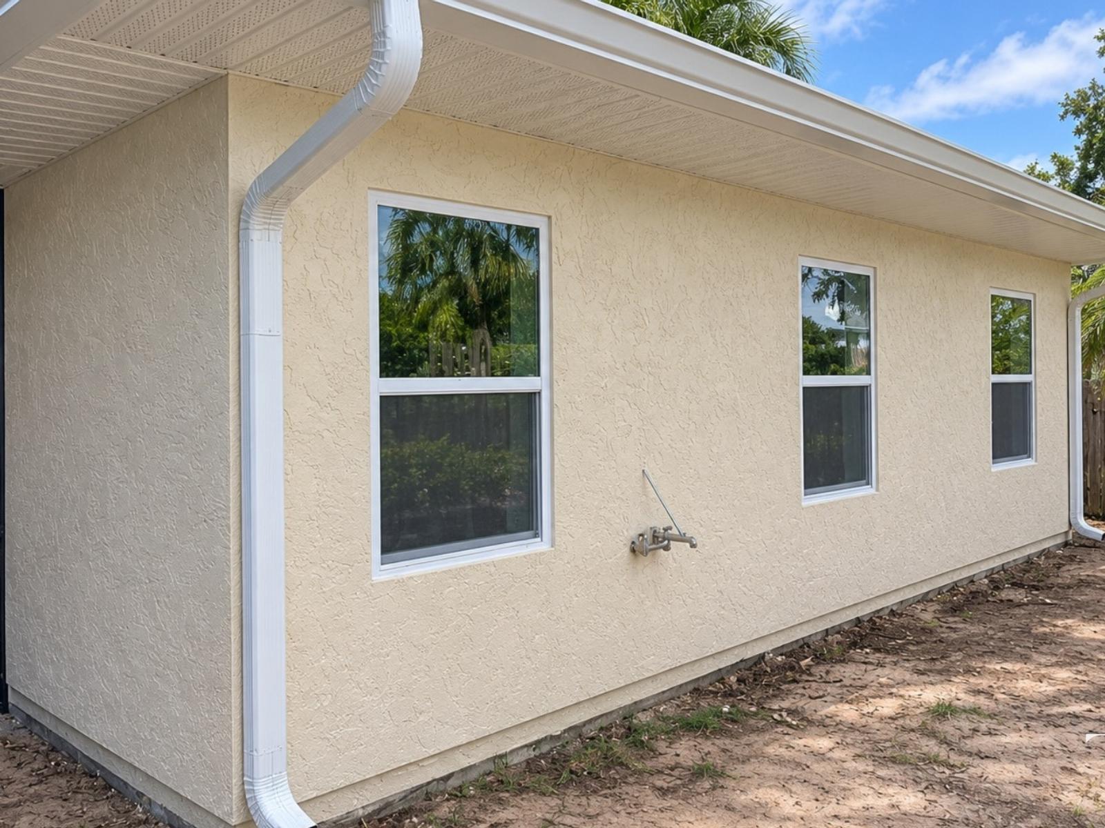 Completed addition exterior with light stucco walls, two windows and a white downspout