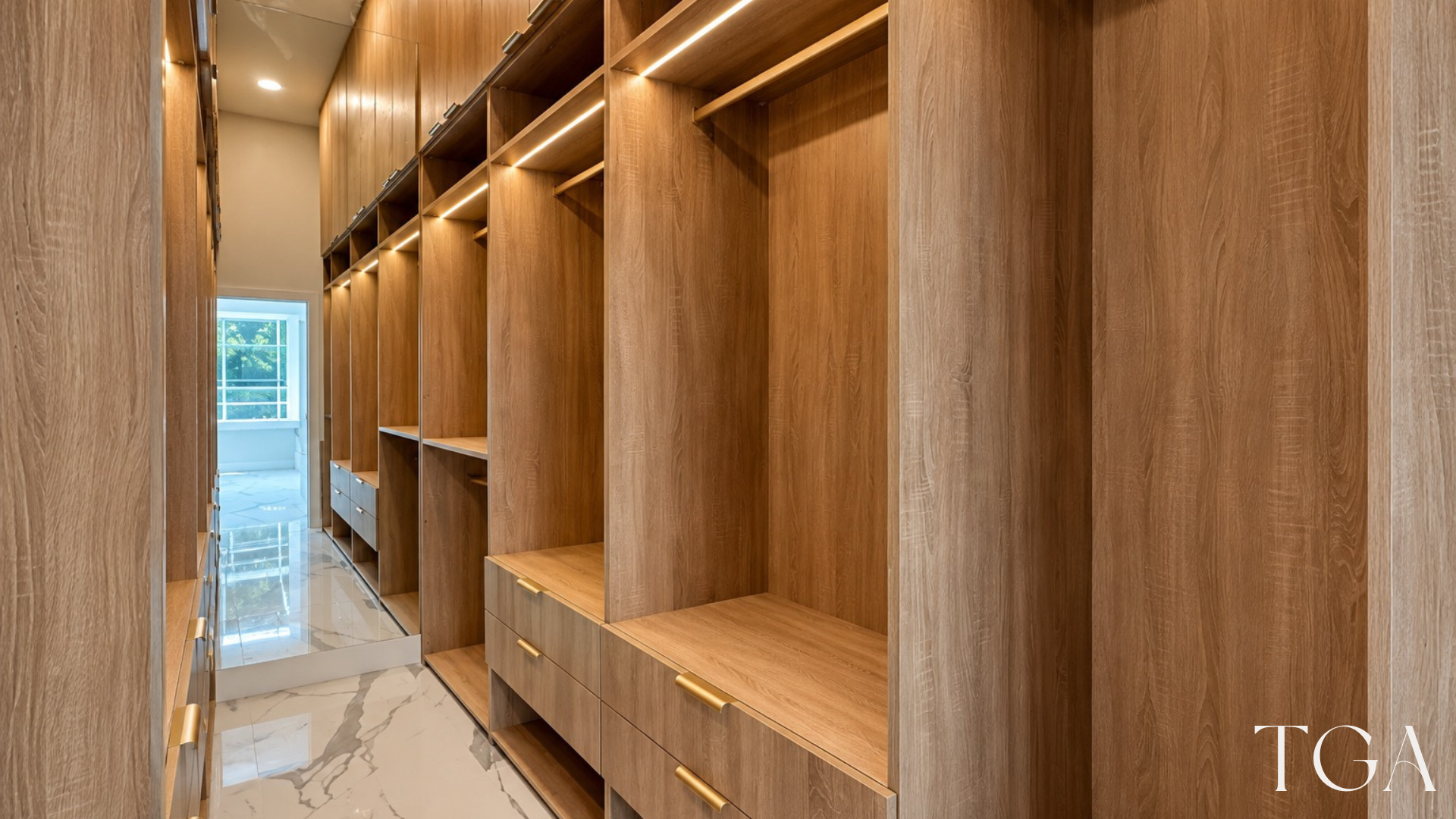 Wood-tone closet storage with illuminated hanging sections, lower drawers, upper cabinets and a full-height mirror.