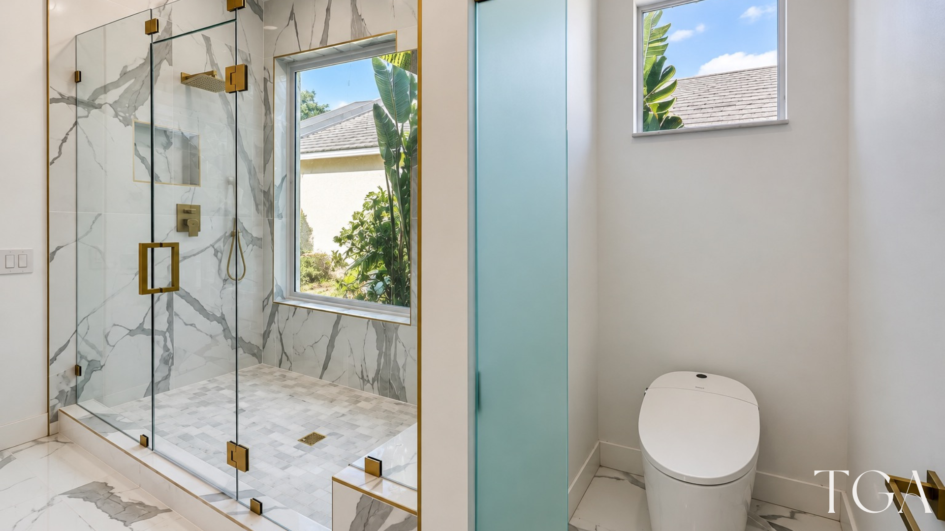 Primary shower beside a toilet area separated by a frosted glass partition, with matching gold hardware.