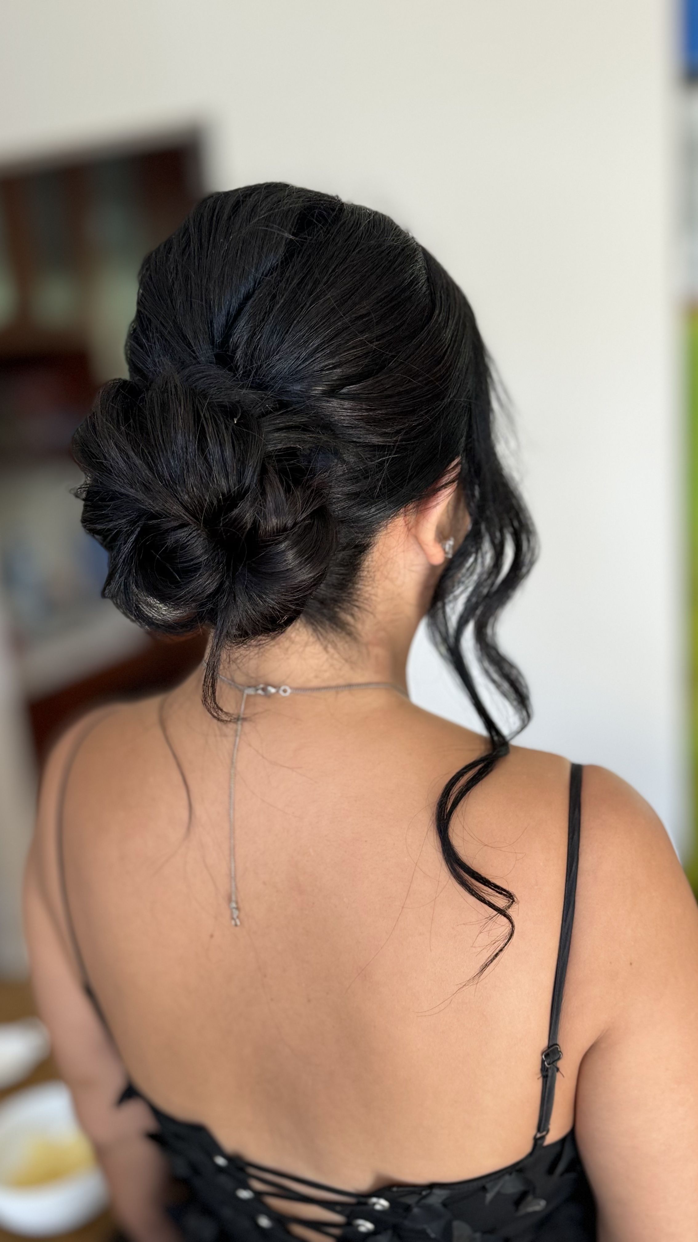 Back view of dark hair styled in a soft low bun with a long loose tendril.